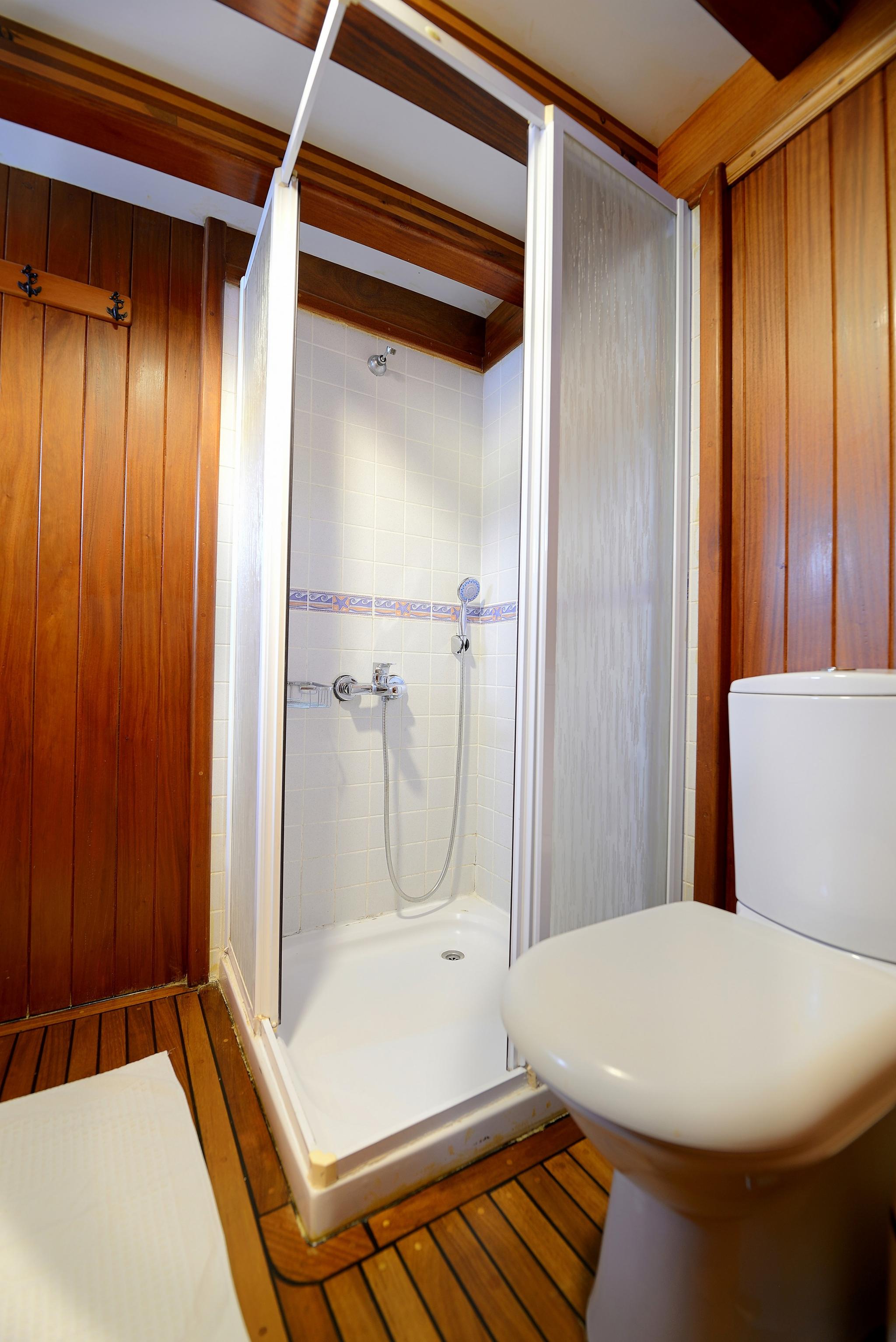 yacht bathroom featuring white shower cubicle with glass doors, toilet, and teak wood paneling