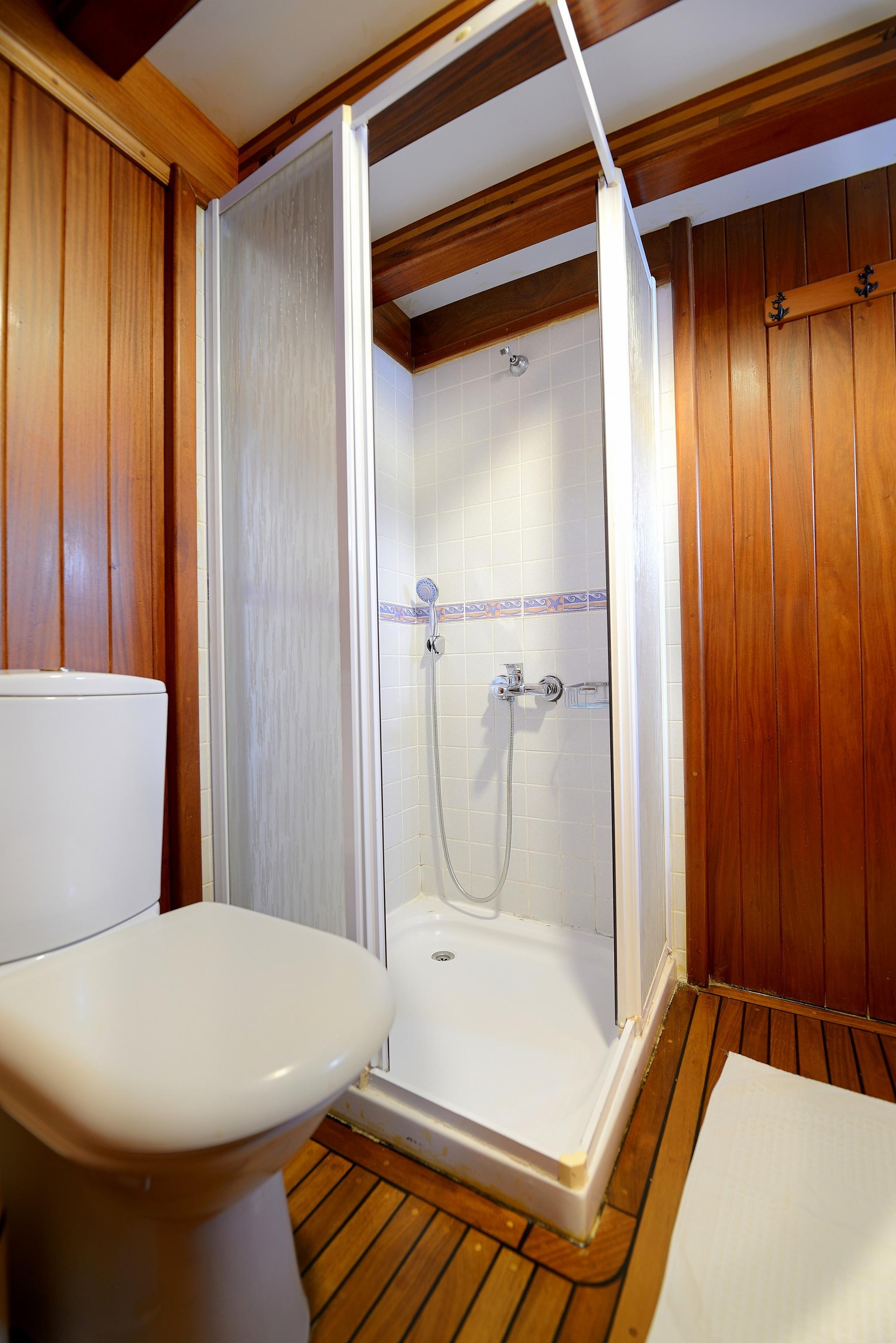 yacht bathroom featuring white shower stall with glass doors, toilet, and teak wood paneling