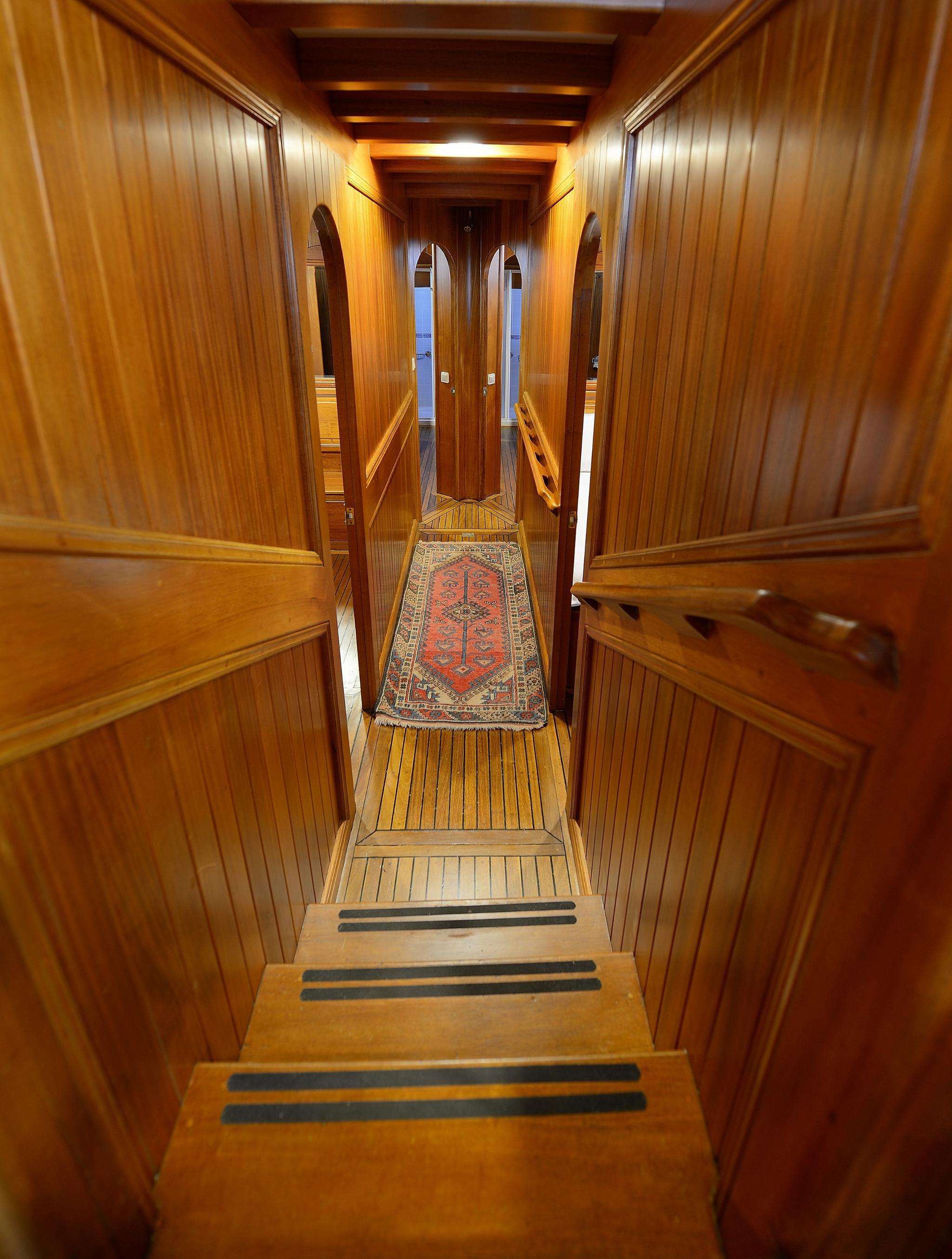 wooden staircase with anti-slip treads leading down to lower deck accommodation corridor with traditional rug