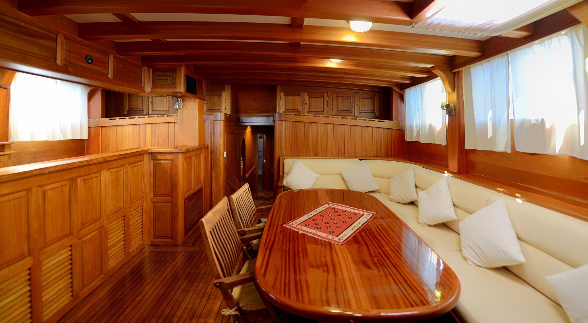 yacht main salon with oval dining table, curved cream upholstery seating and traditional wood paneling