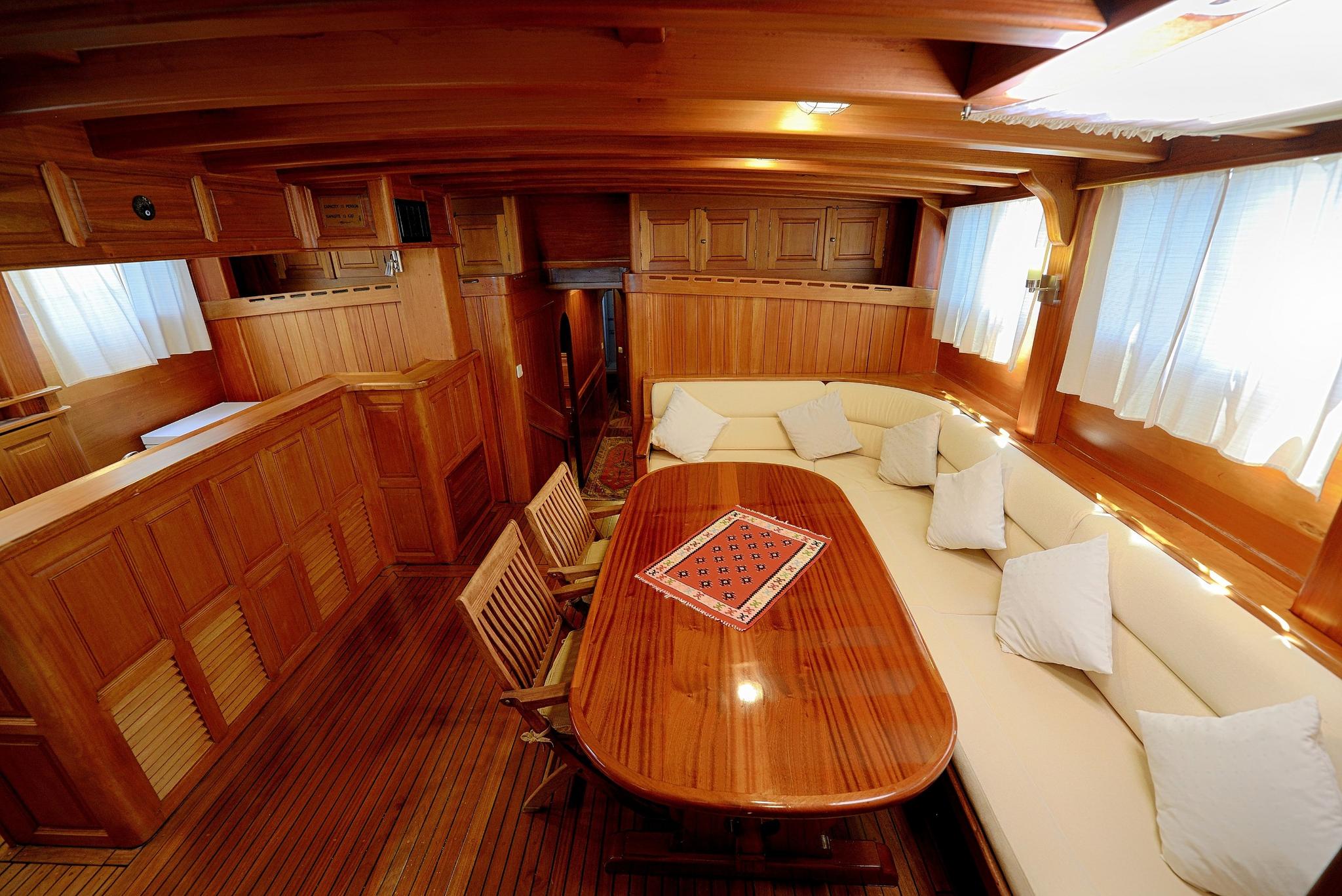 yacht main salon with curved white seating, oval wooden dining table and rich wood paneling