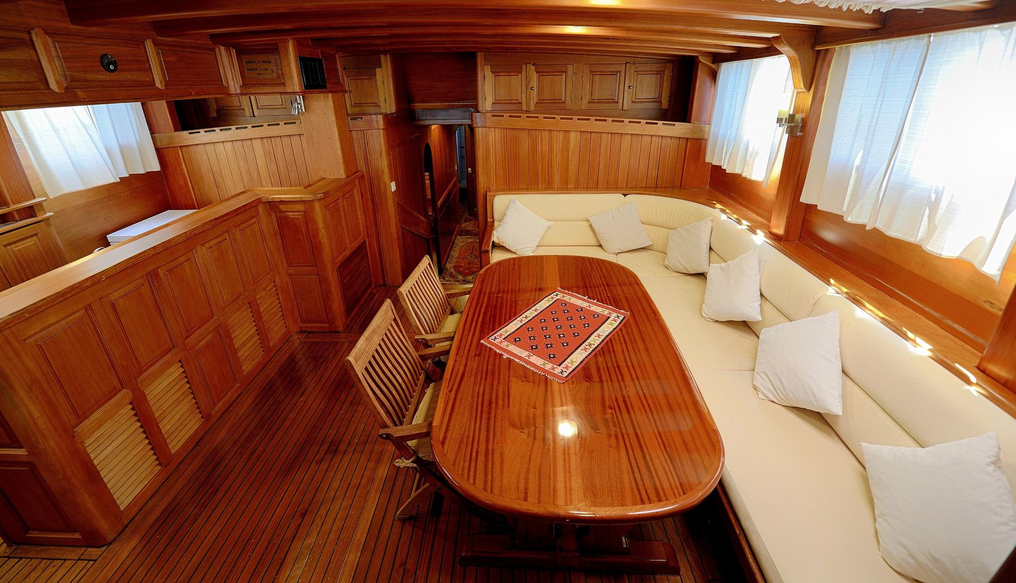 yacht interior salon with curved cream seating, oval dining table and wood paneling