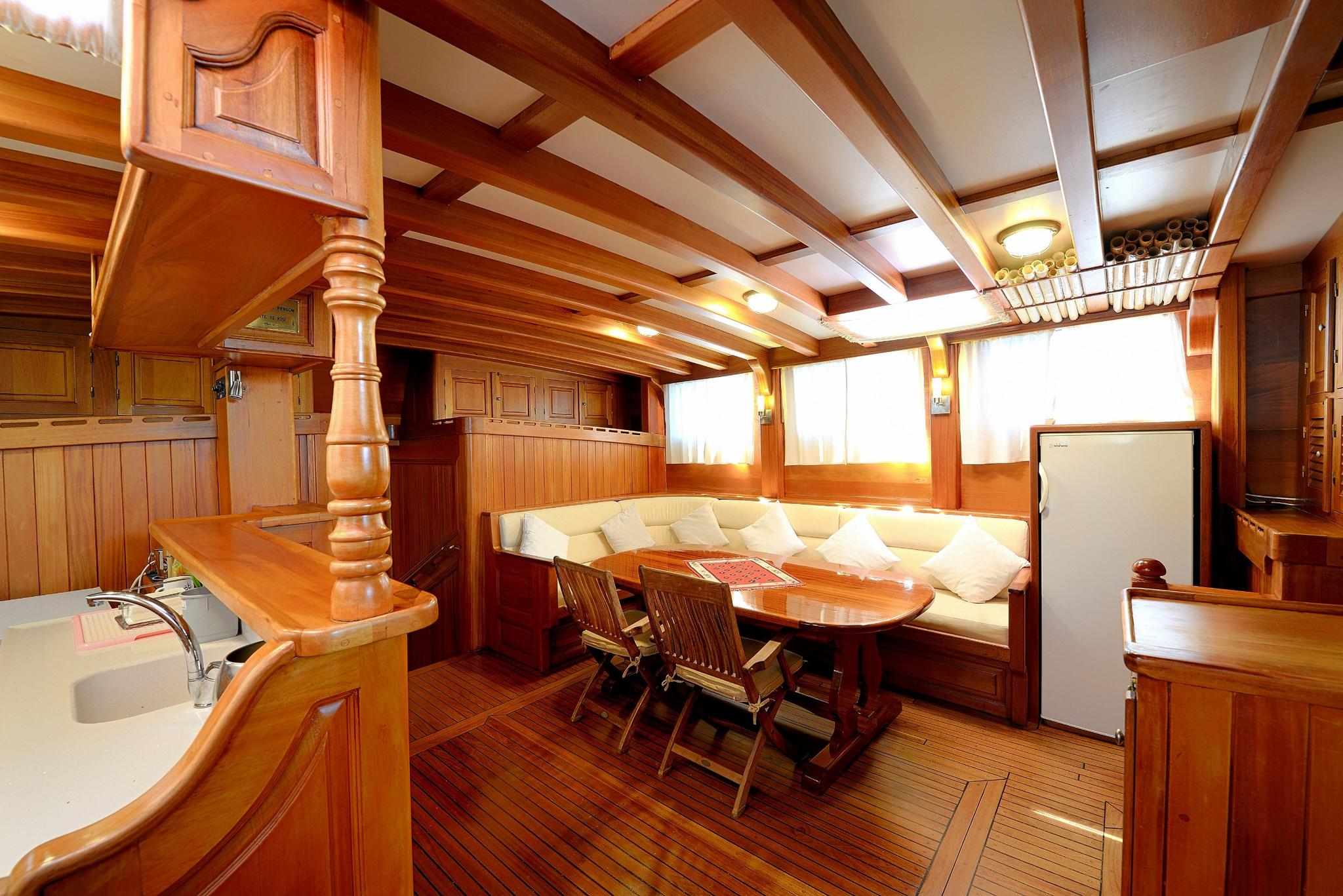 yacht interior salon with U-shaped seating, dining table, galley with sink and wooden cabinetry