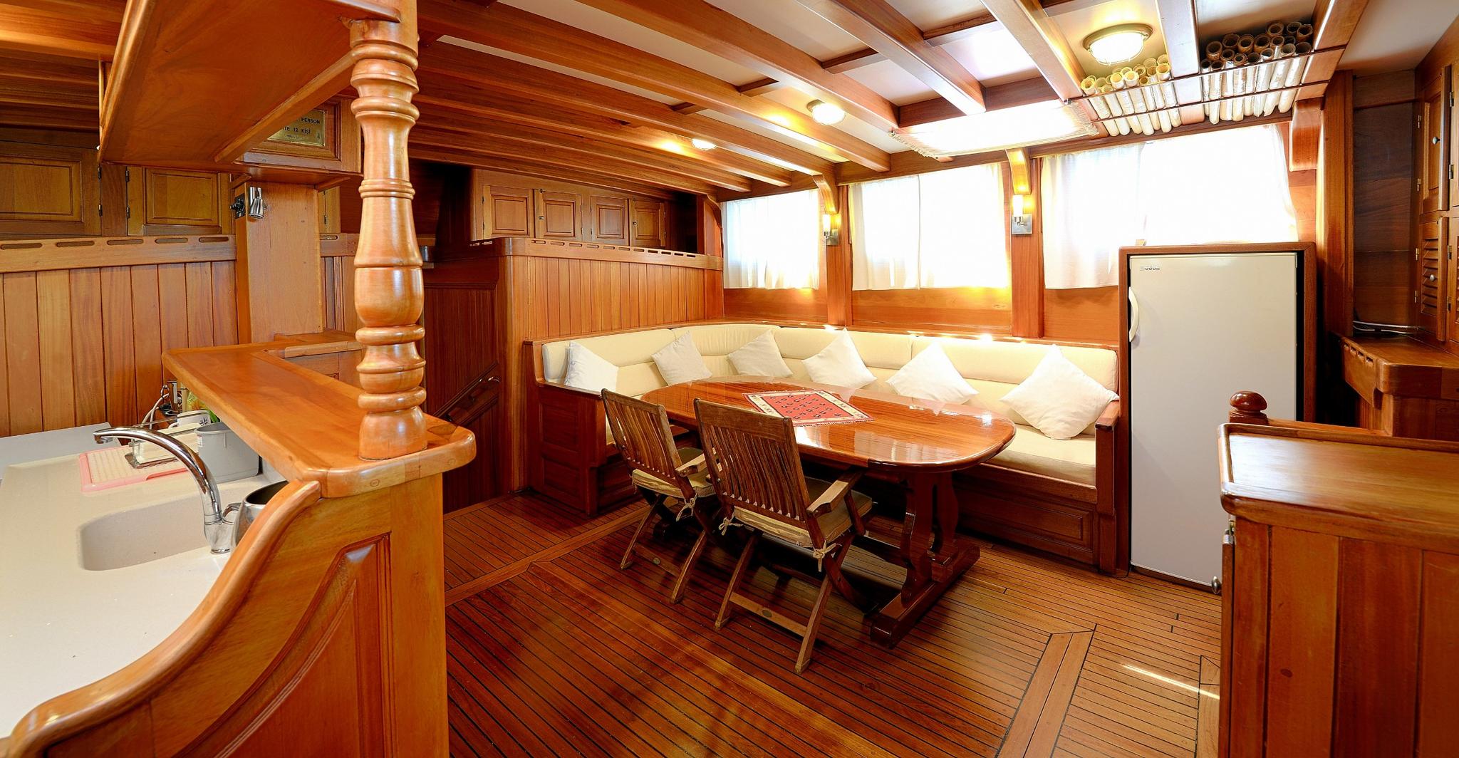 yacht main salon interior with wooden dining table, built-in seating, galley and traditional teak woodwork