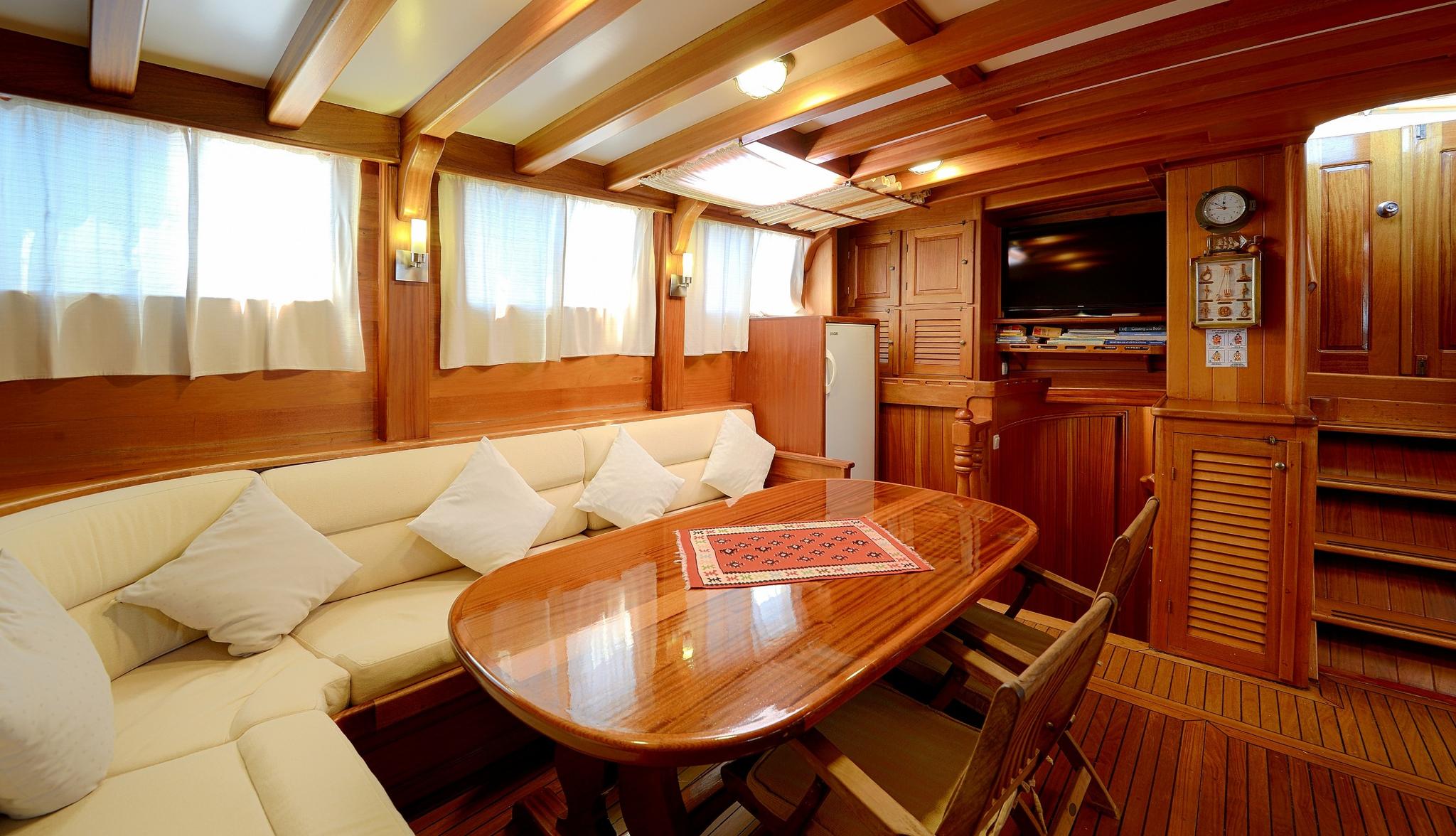 yacht main salon interior with cream U-shaped banquette seating, oval dining table, and entertainment center