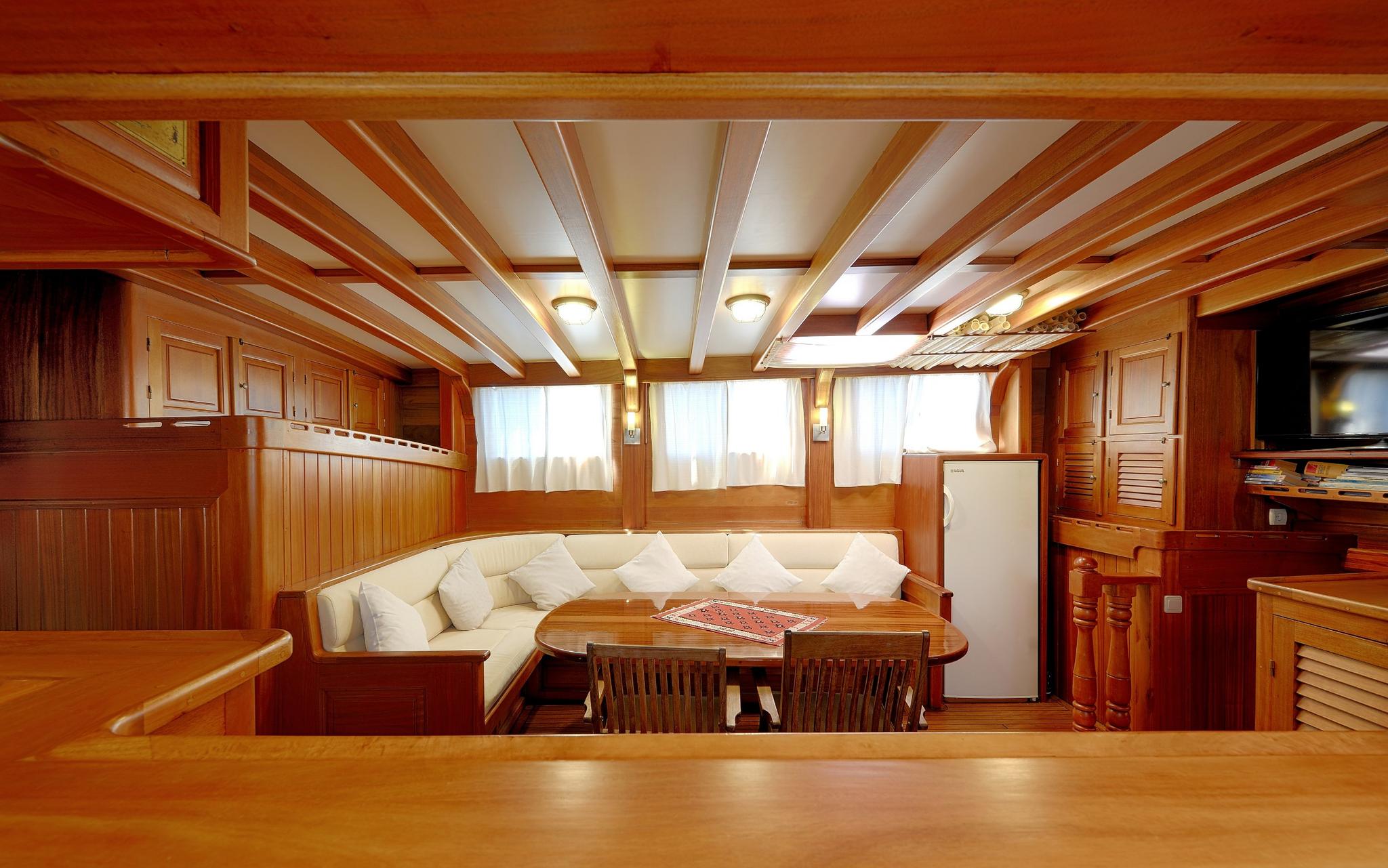 yacht interior salon with wraparound cream seating, wooden dining table and traditional wood paneling