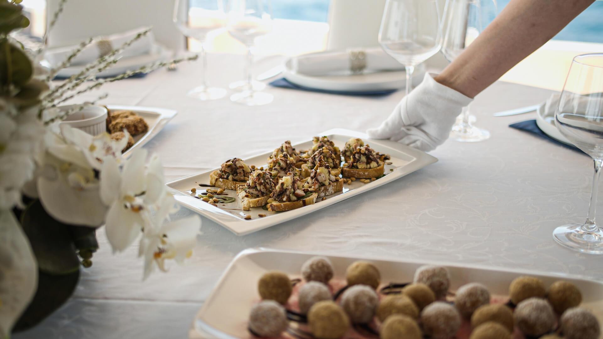 crew member in white gloves serving stuffed appetizers and chocolate truffles on yacht dining table