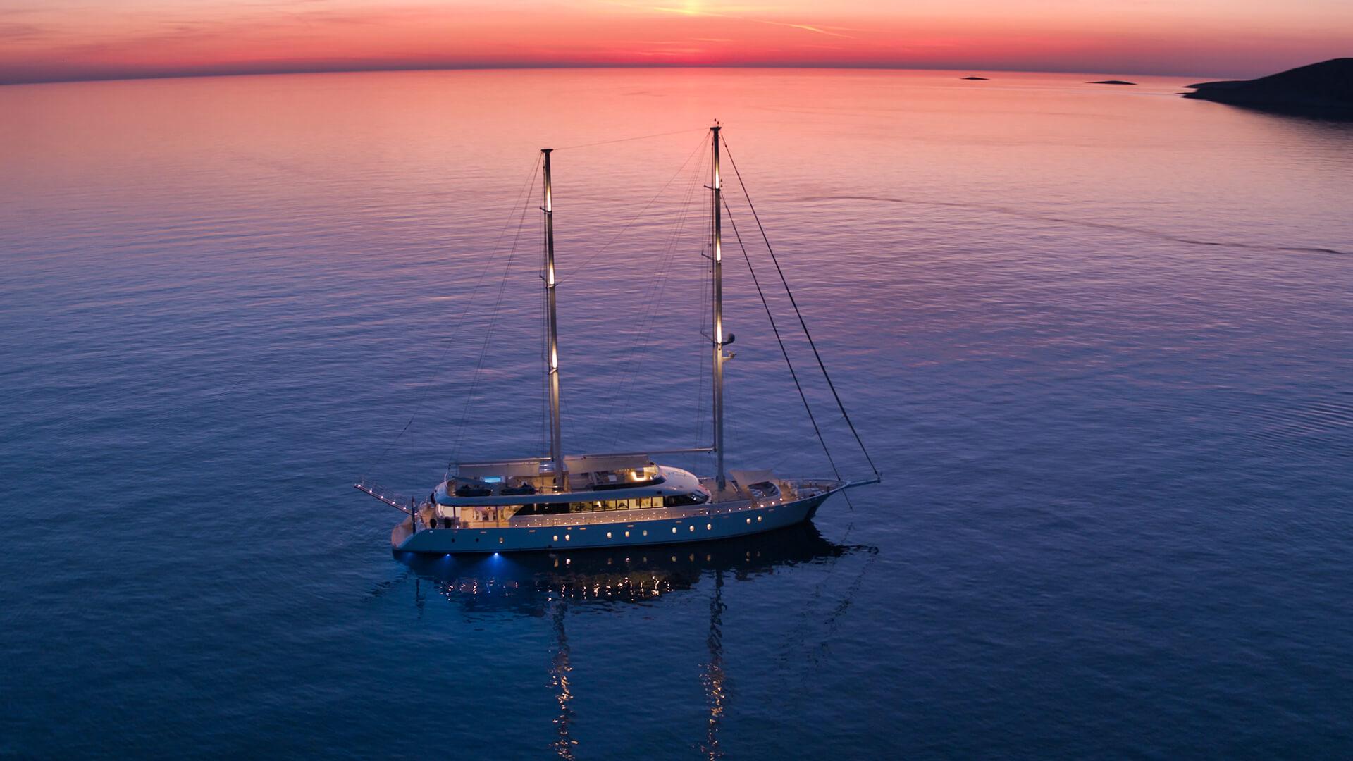 luxury gulet yacht anchored in calm waters at sunset with deck lighting and two masts