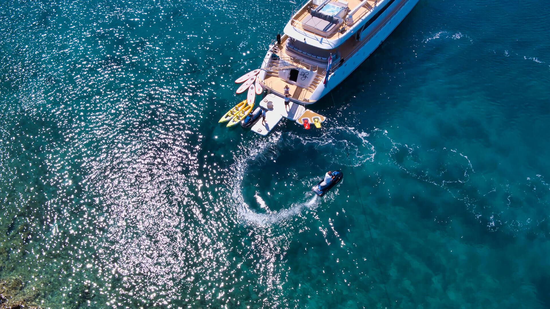 aerial view of luxury yacht anchored in turquoise water with jet ski and water sports equipment