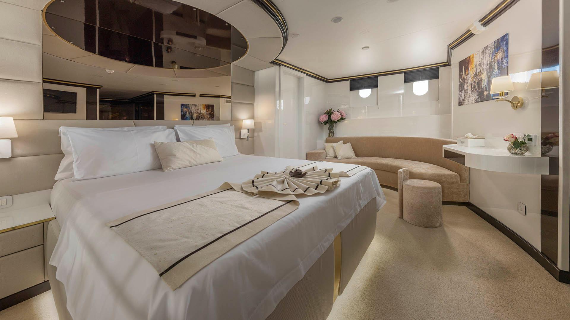 spacious yacht master cabin featuring king bed, curved seating area, mirrors and neutral decor