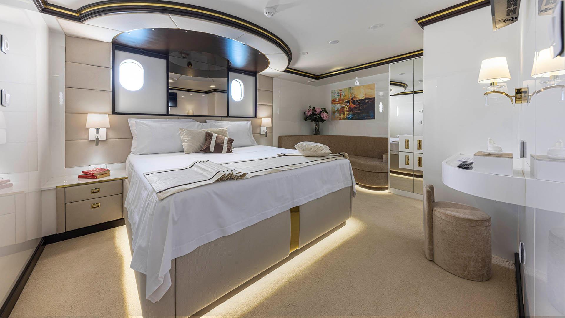 yacht master cabin with king bed, curved ceiling mirror, two portholes and vanity desk
