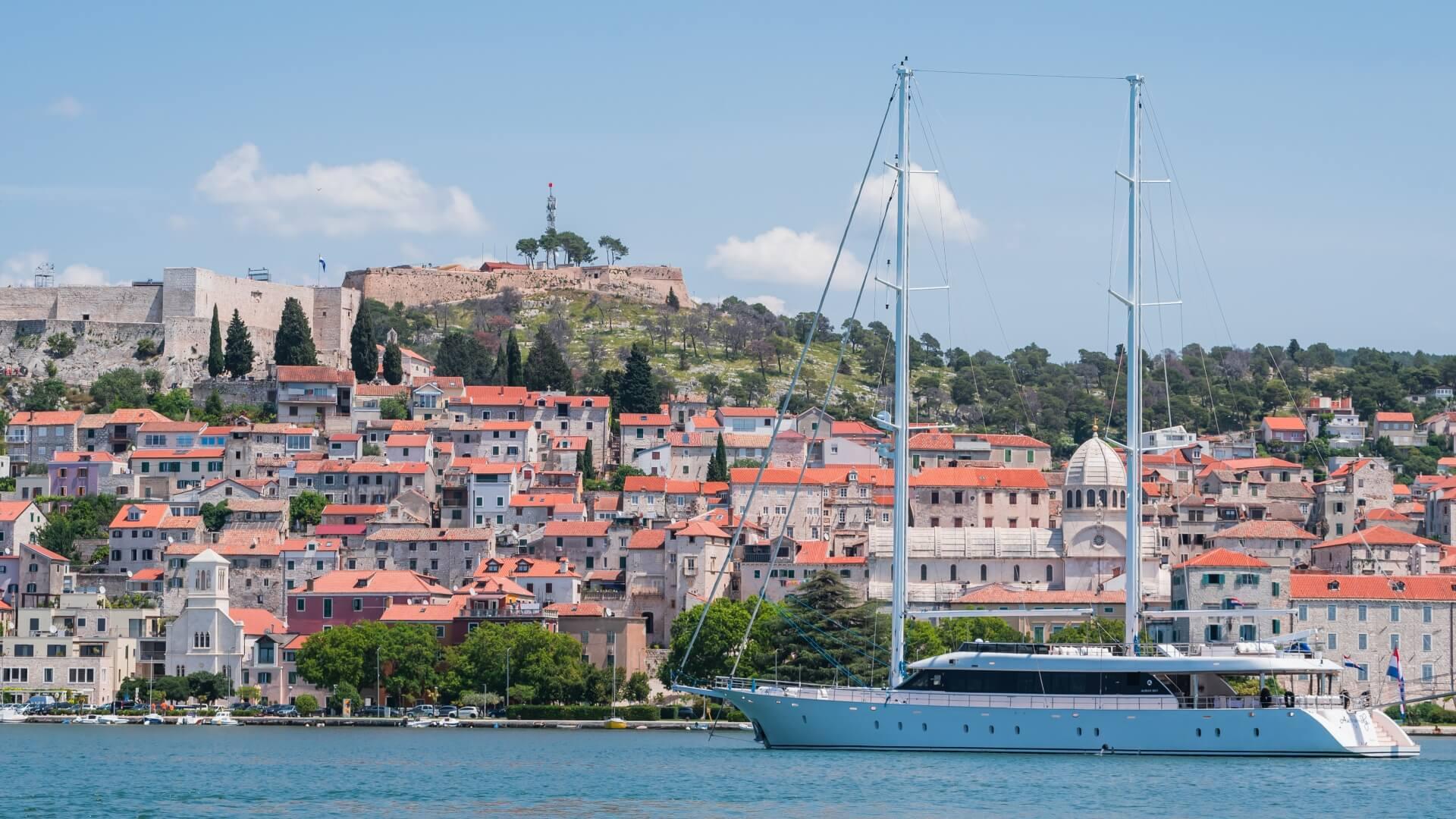 luxury sailing yacht at anchor in Mediterranean harbor with Croatian historic town backdrop