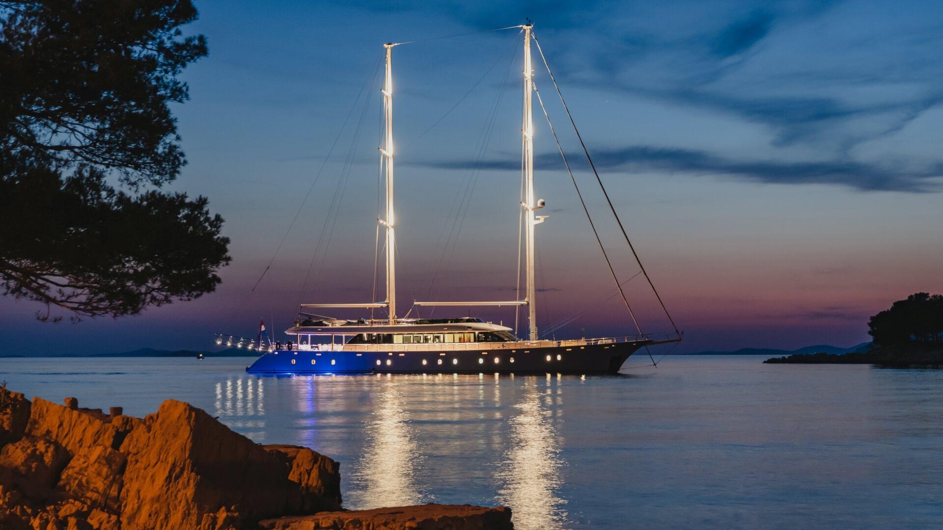 luxury gulet with two masts anchored in calm bay at twilight with exterior lighting