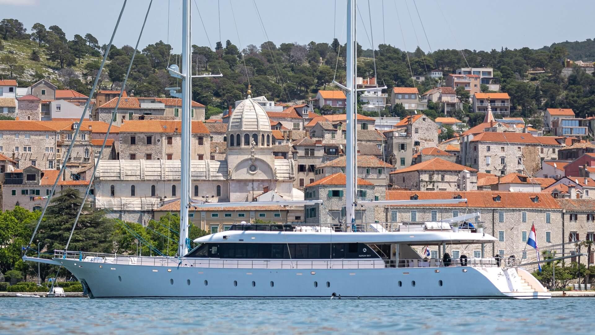 Large white sailing yacht with two masts anchored in historic Croatian harbor with stone buildings