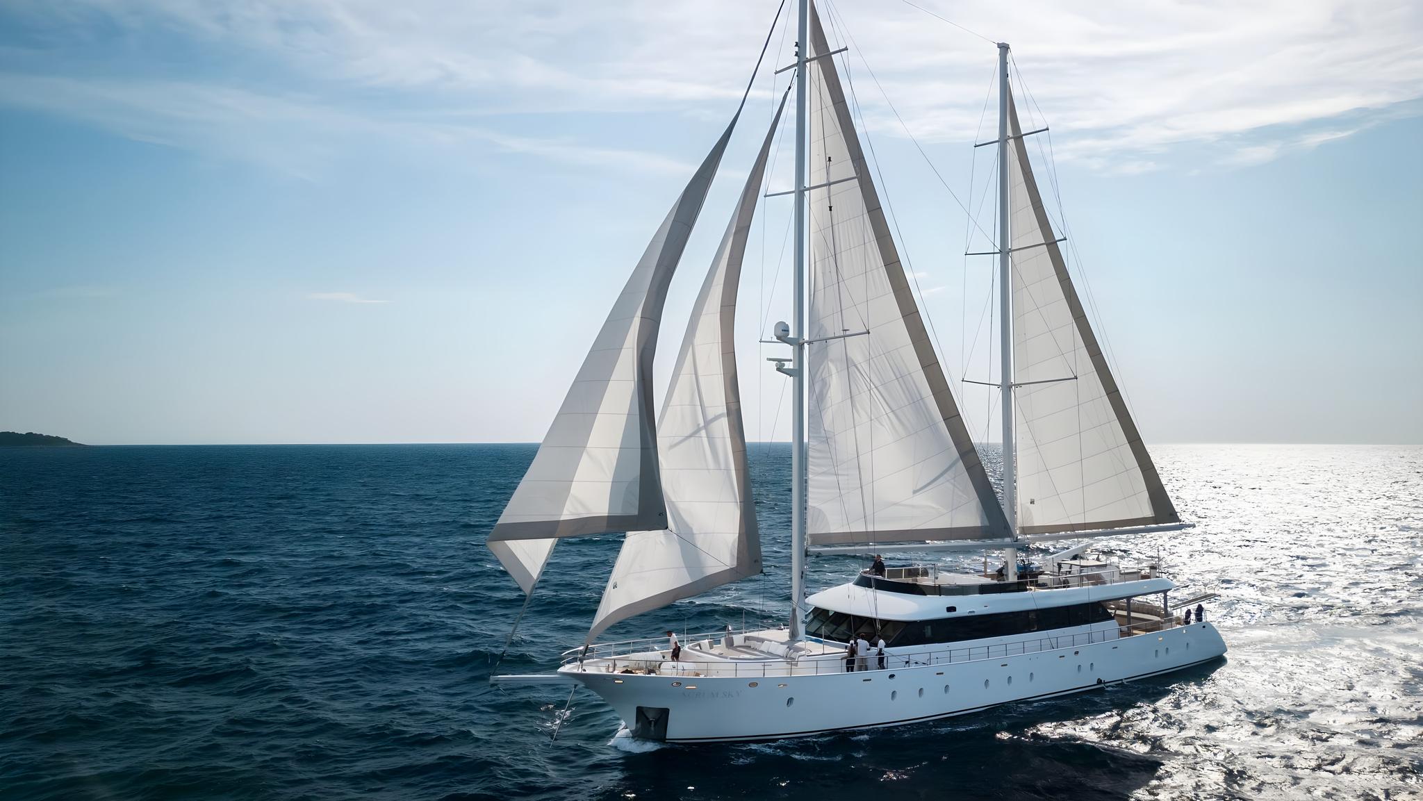 white sailing yacht with full white sails deployed cruising on blue water with crew visible on deck