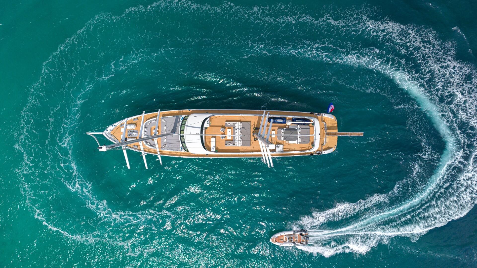 aerial view of traditional wooden gulet yacht circling in crystal clear turquoise waters with tender boat