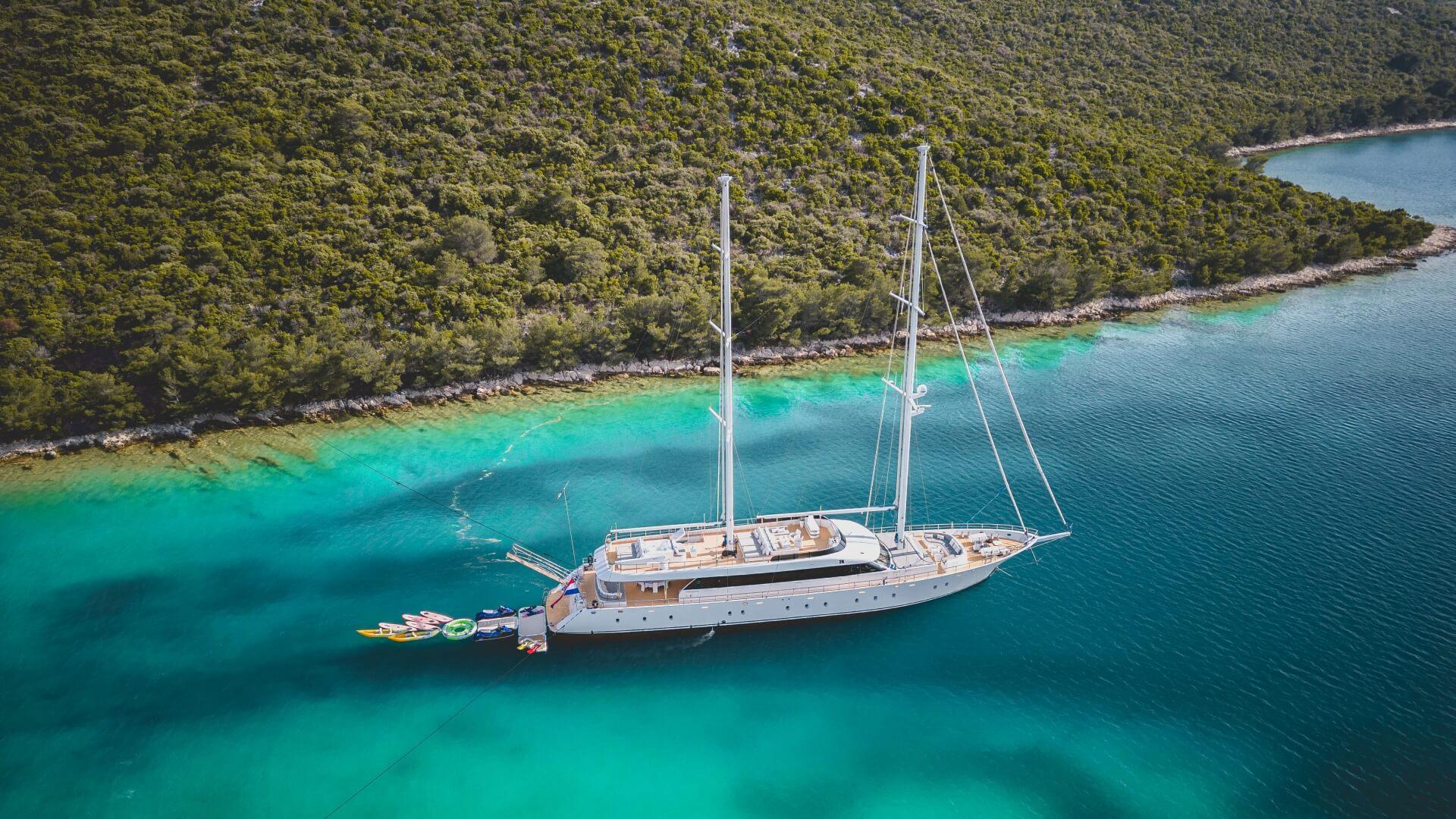 aerial view of white gulet yacht anchored in crystal clear turquoise bay with water toys deployed