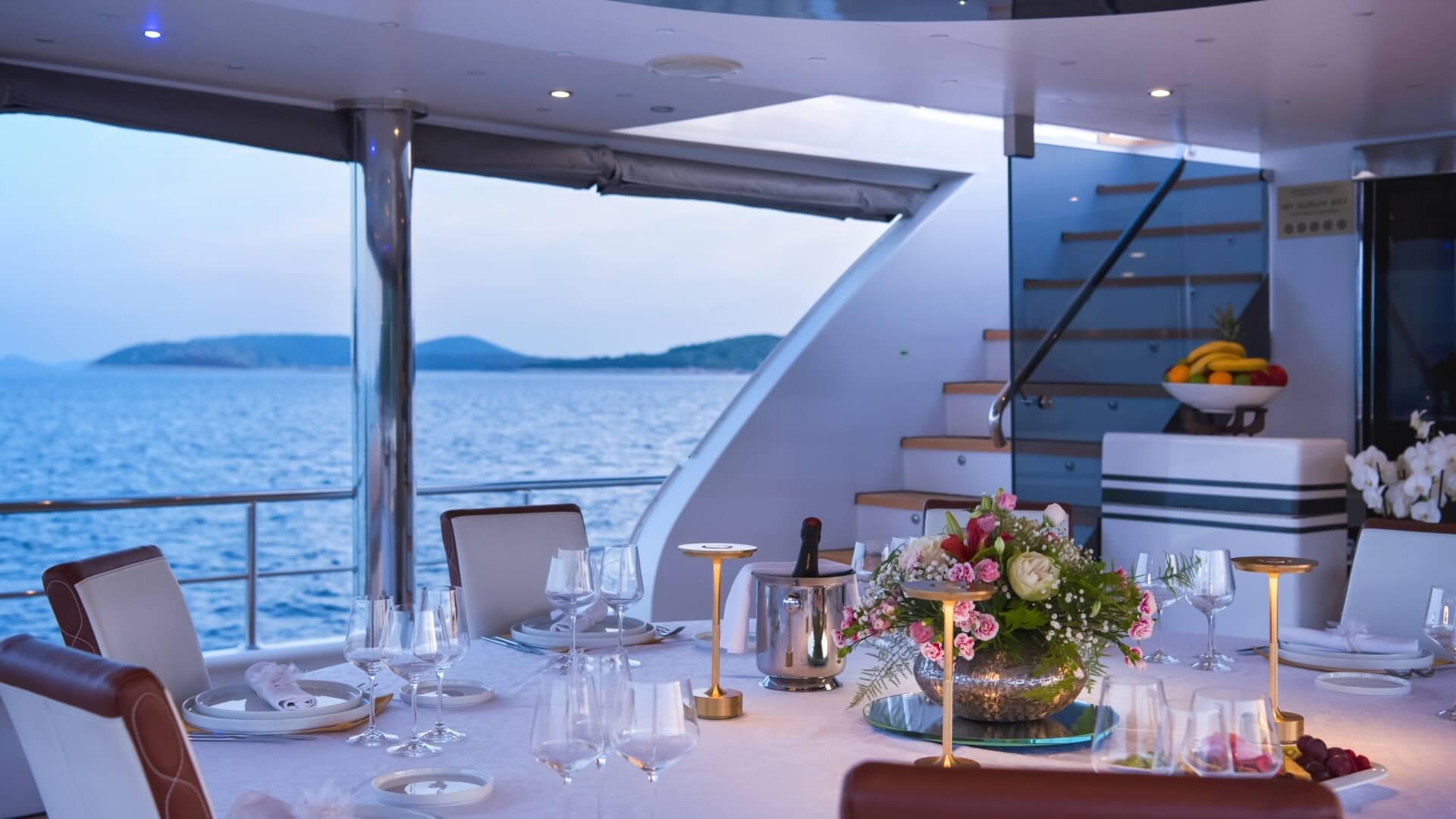 elegant yacht dining area with set table, wine glasses, floral arrangement and ocean views