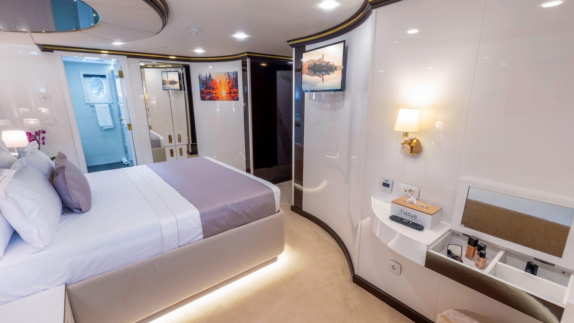 luxury yacht cabin featuring white double bed, curved ceiling design, ensuite bathroom, and built-in storage