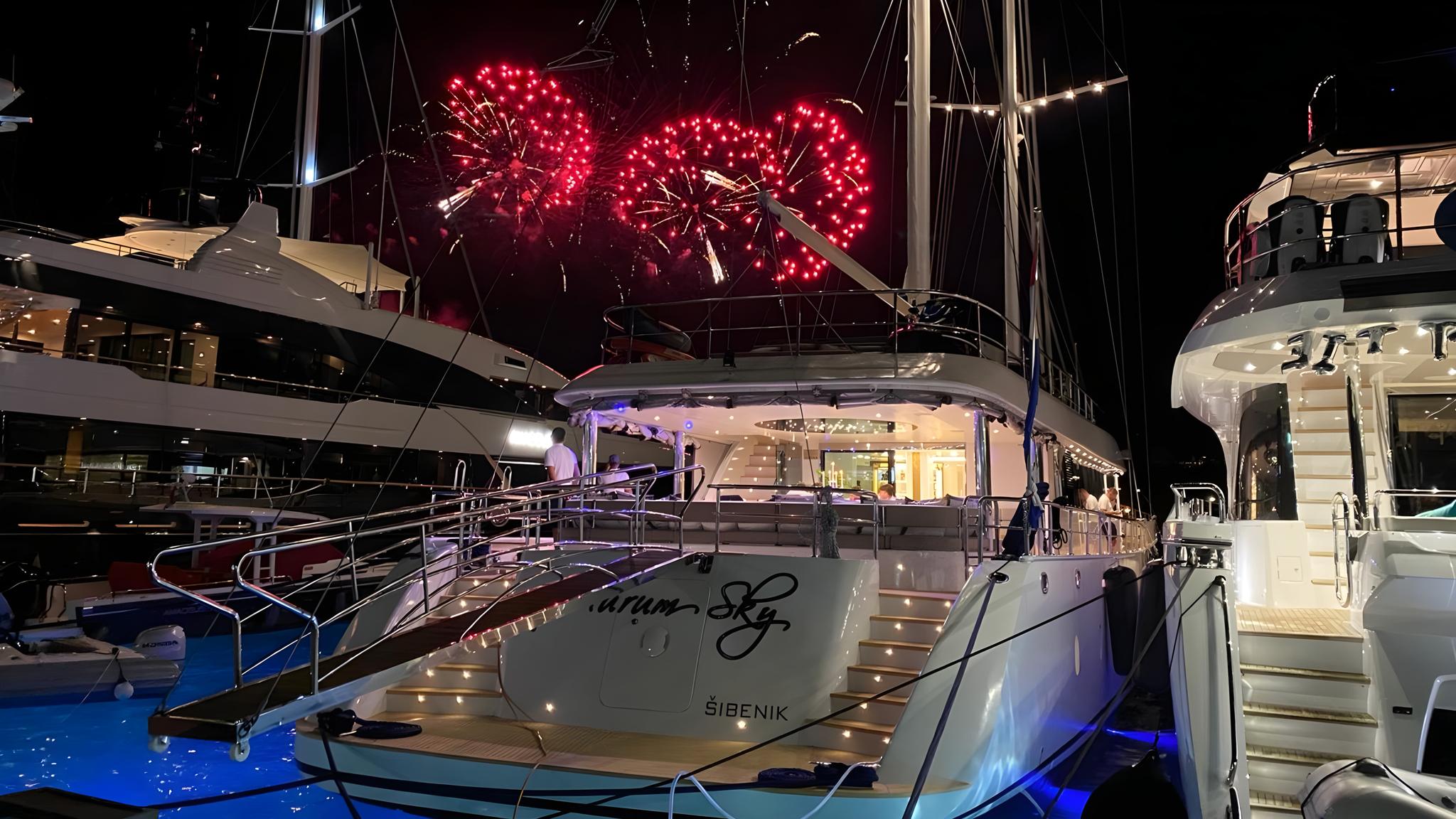 luxury yacht stern deck illuminated at night with red fireworks bursting overhead in marina