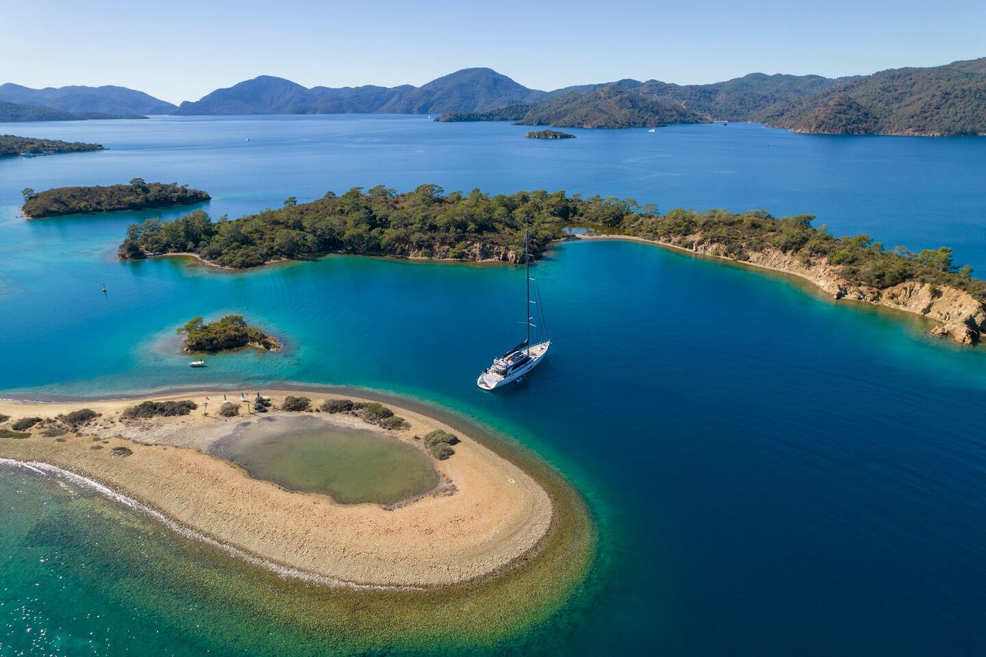 Aerial view of sailing yacht anchored in protected turquoise bay surrounded by forested islands
