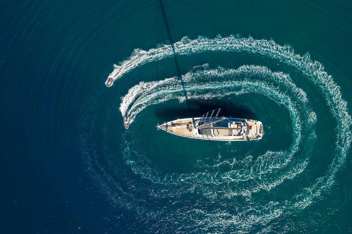 aerial view of luxury yacht creating dramatic circular wake patterns in turquoise water