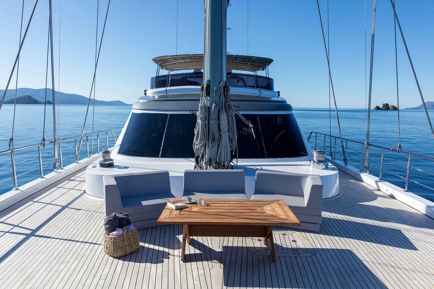 bow deck seating area with white built-in sofa, teak coffee table and central mast