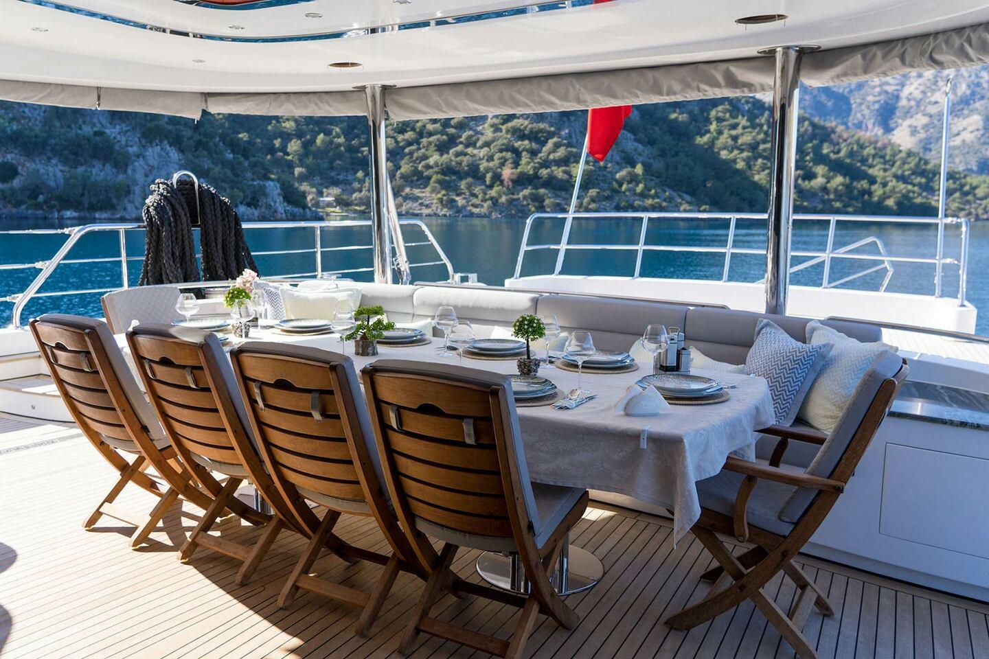 yacht aft deck dining area with white tablecloth, folding teak chairs, and built-in seating
