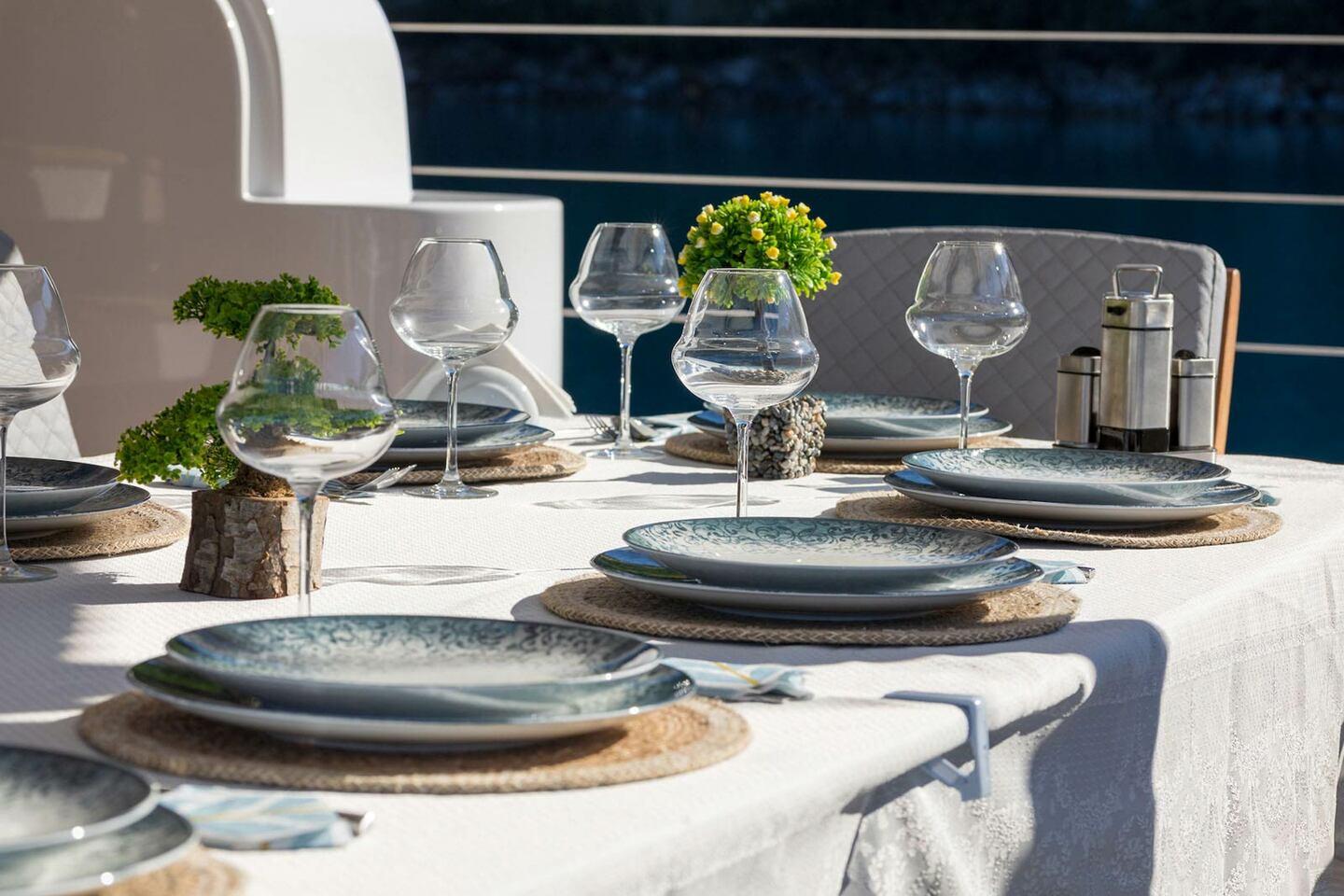 elegant yacht dining table set with blue speckled plates, wine glasses and natural decorations