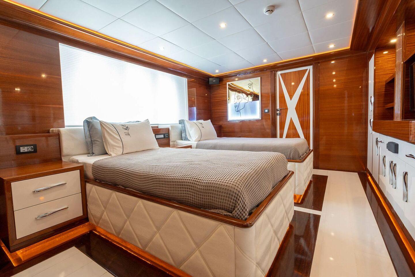 yacht twin cabin with cream quilted bed bases, wood paneling and artwork
