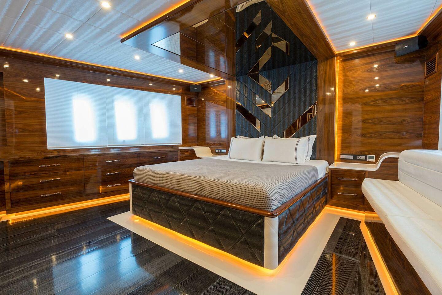 Master cabin featuring king bed with quilted base, walnut paneling, LED strip lighting and three windows