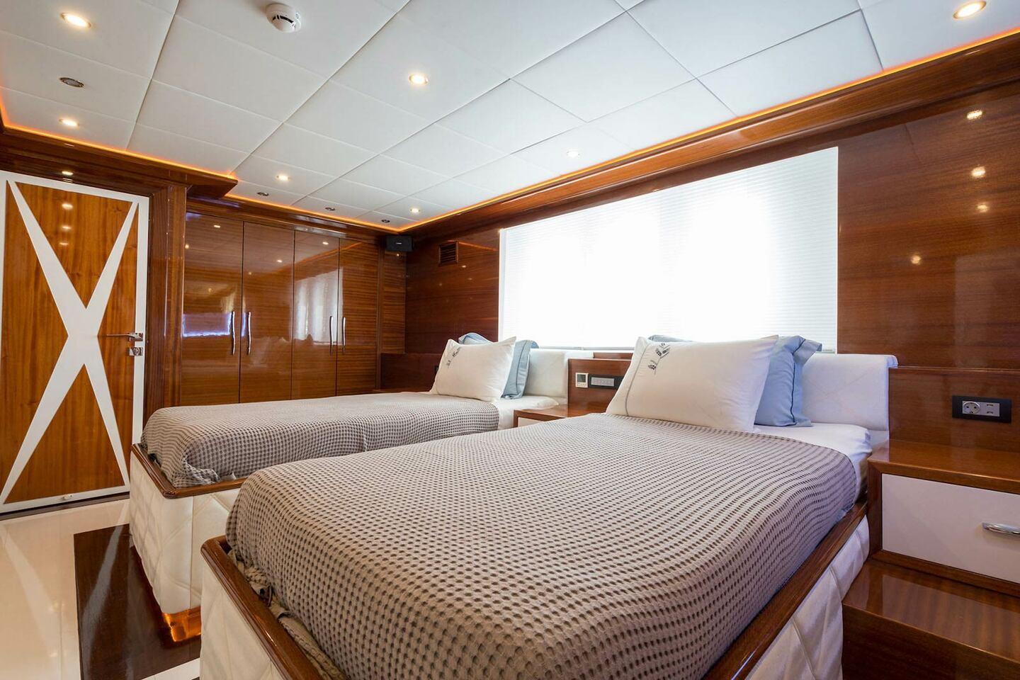 yacht twin cabin with two beds, grey checkered bedding and warm wood interior