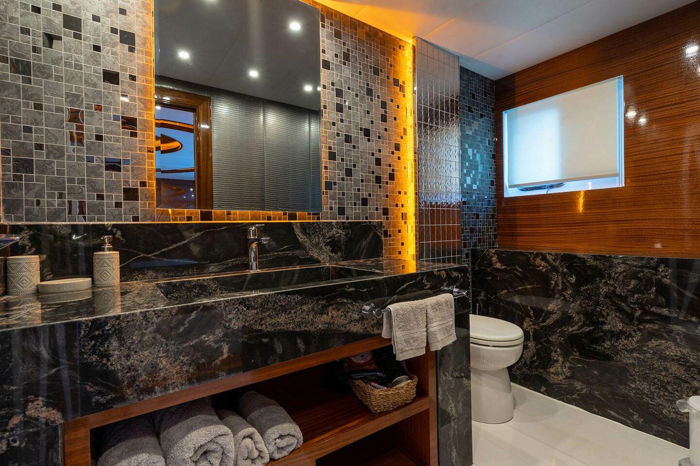 Yacht bathroom featuring black marble vanity, mosaic tile walls, and modern fixtures