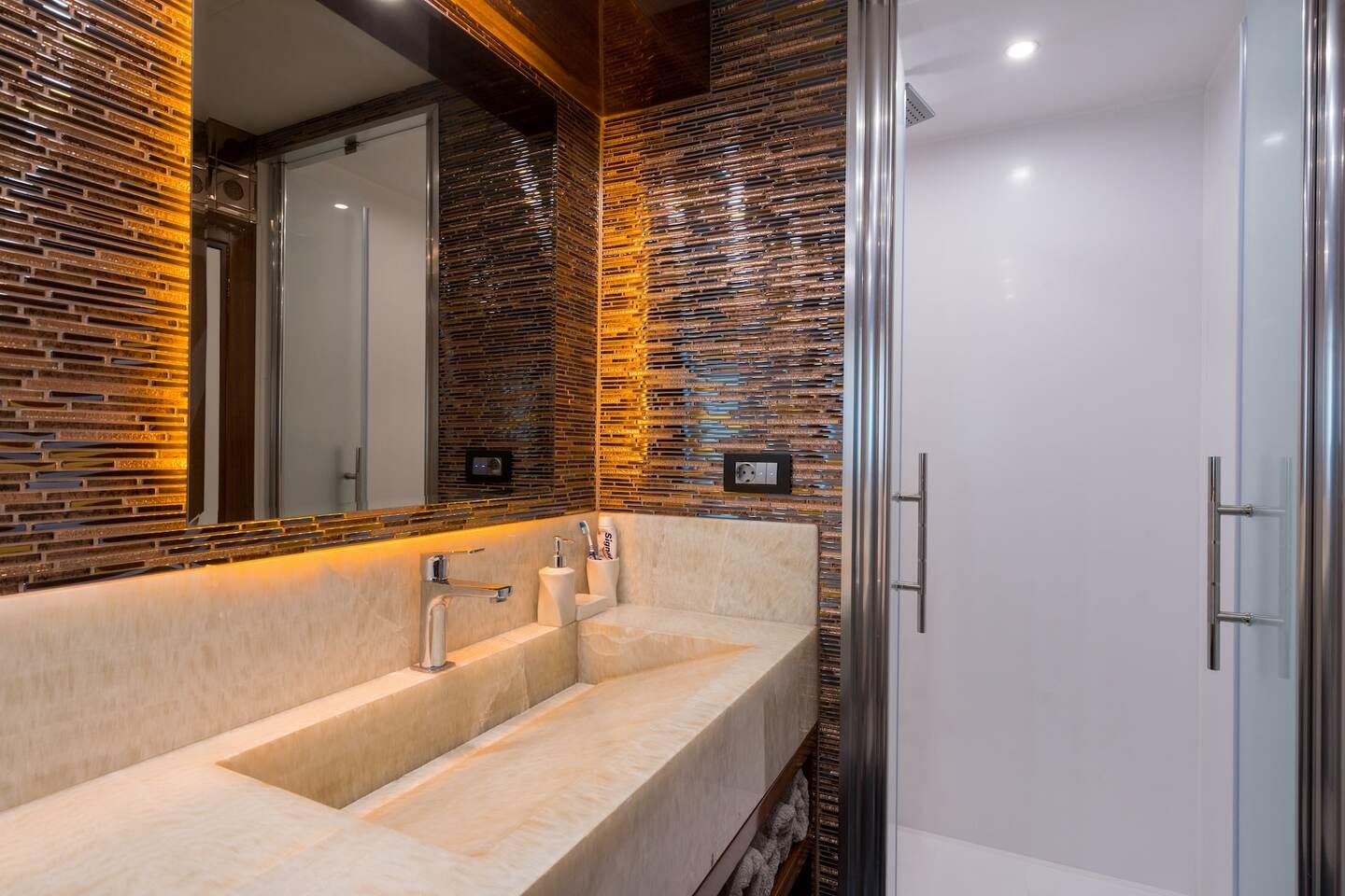 yacht bathroom featuring marble vanity with integrated sink, mosaic tile wall, and glass shower door