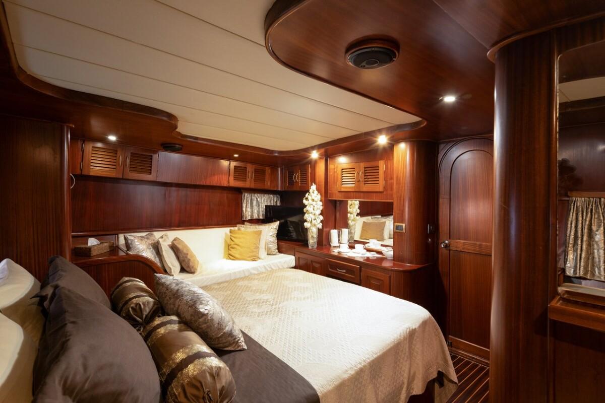 yacht cabin interior featuring double bed with cream bedding and extensive mahogany wood cabinetry