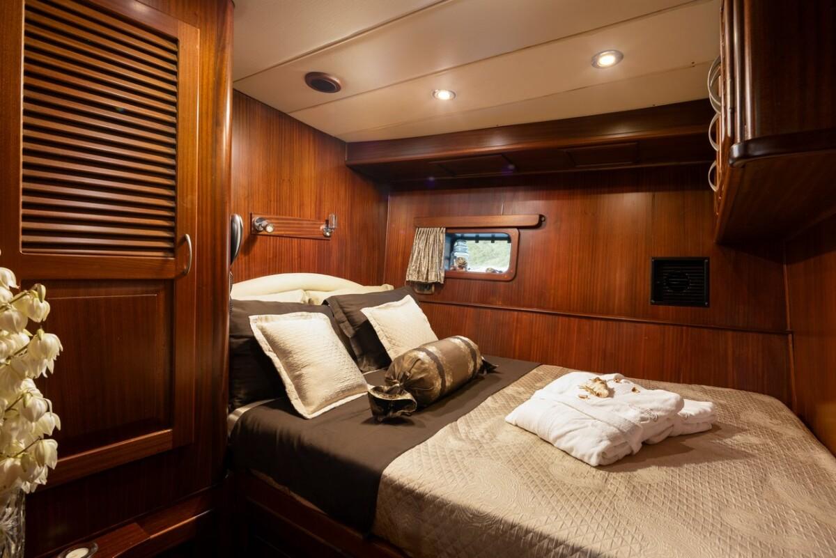 yacht cabin interior with double bed, wooden walls, porthole window and white towels