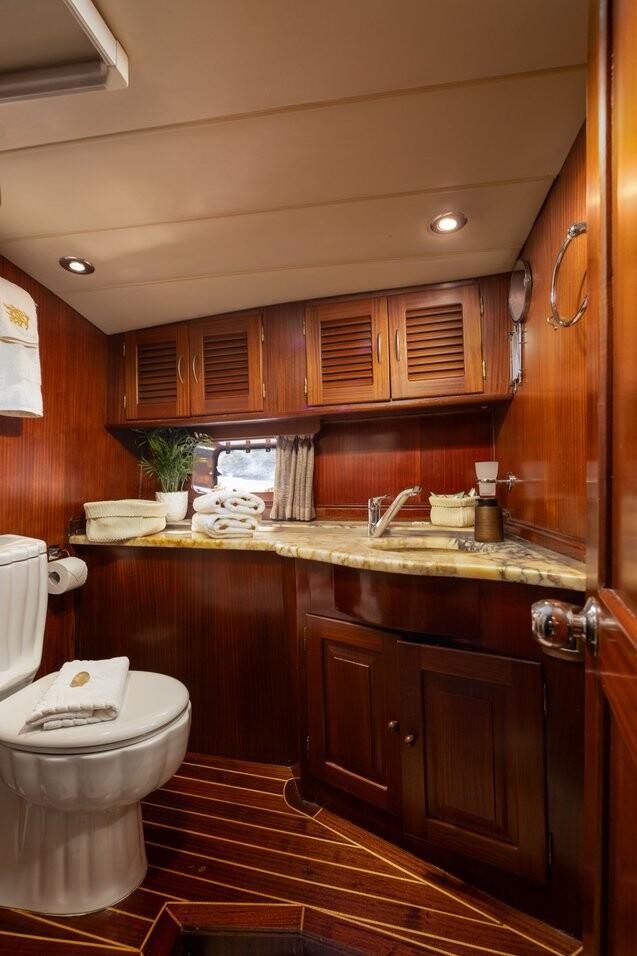compact yacht bathroom featuring white toilet, marble countertop vanity with sink and teak wood cabinetry