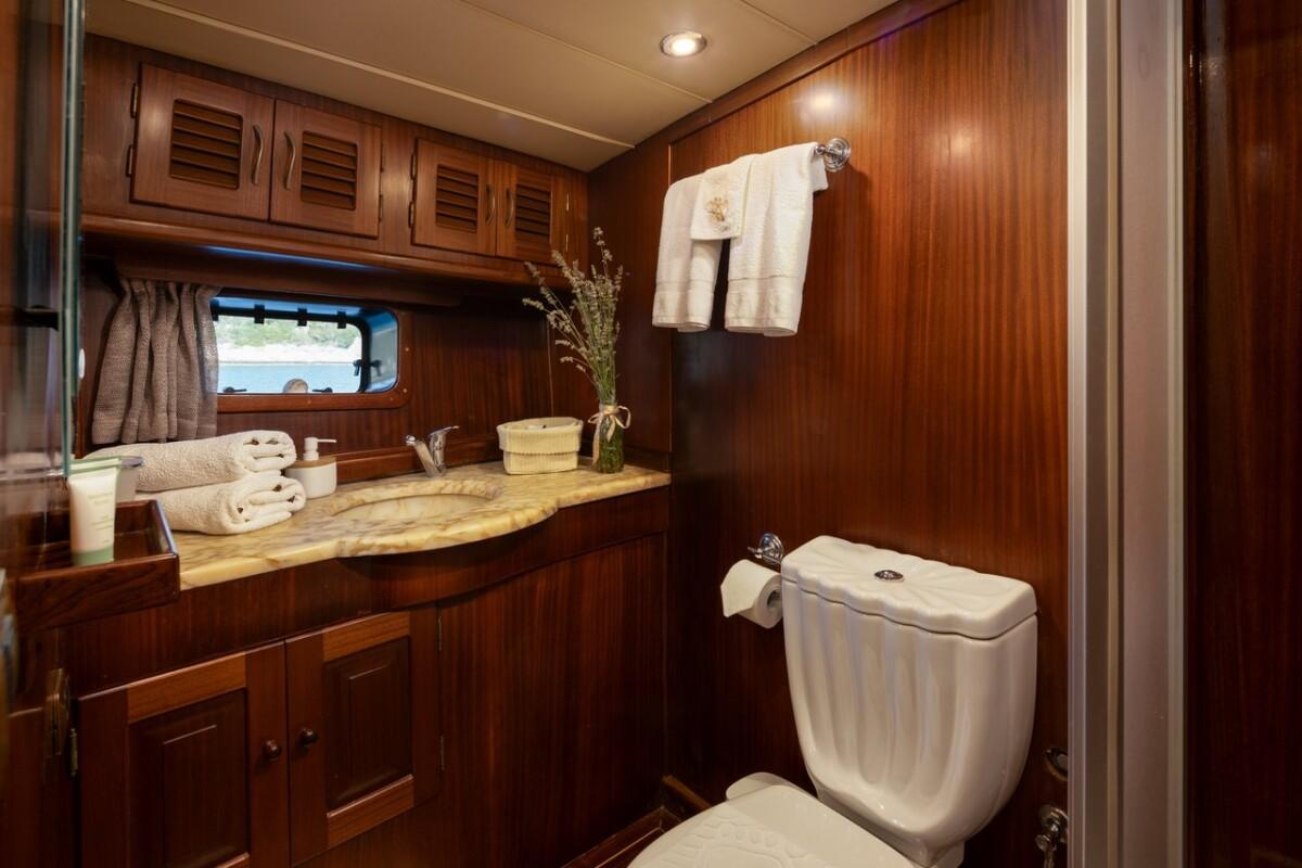 yacht bathroom featuring marble countertop vanity, toilet, towels and wooden cabinetry