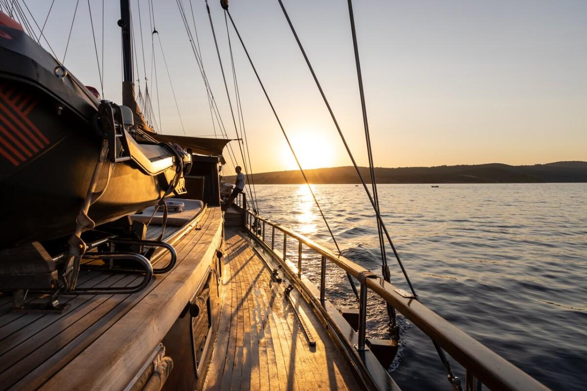 Gulet side deck with wooden planking, rigging lines and sunset over water