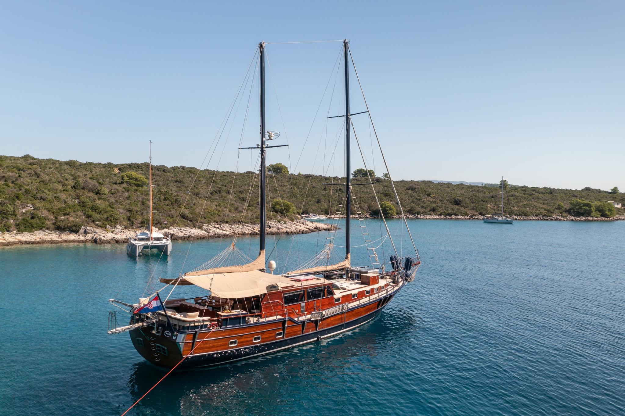 Traditional wooden gulet with two masts anchored in crystal clear turquoise Mediterranean bay