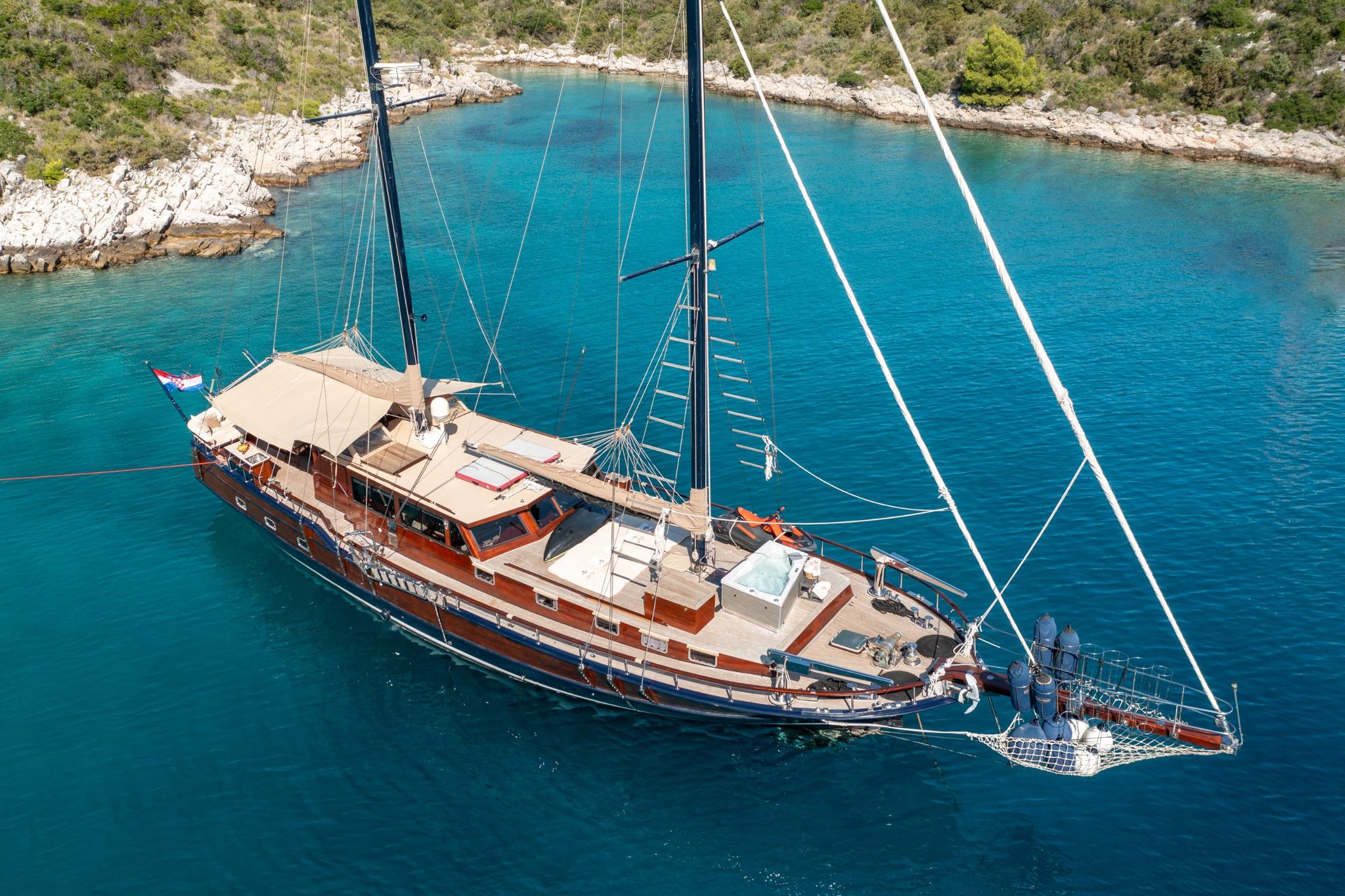 aerial view of traditional wooden gulet with two masts anchored in crystal clear turquoise Mediterranean bay