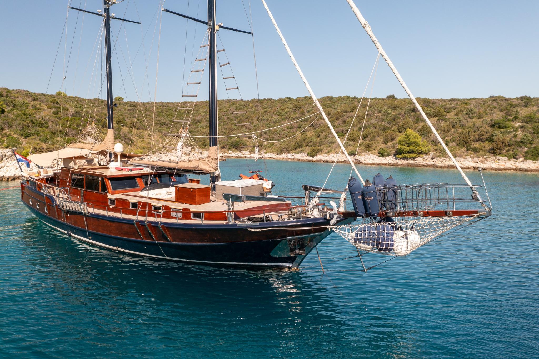 traditional wooden gulet with two masts anchored in turquoise Mediterranean bay with rocky coastline