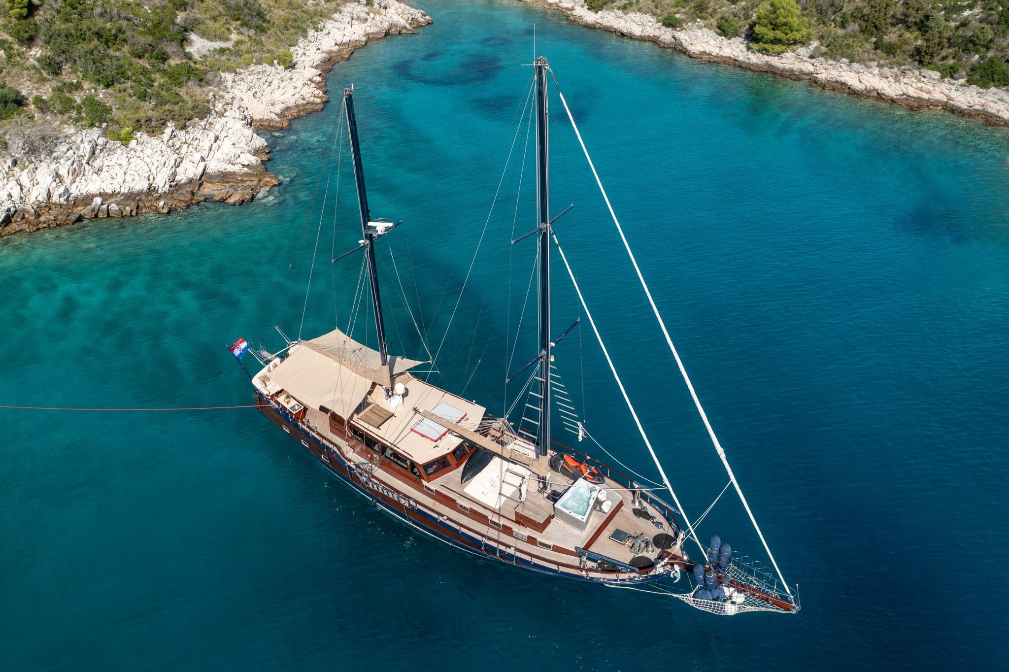 aerial view of traditional wooden gulet yacht anchored in secluded turquoise bay surrounded by rocky coastline