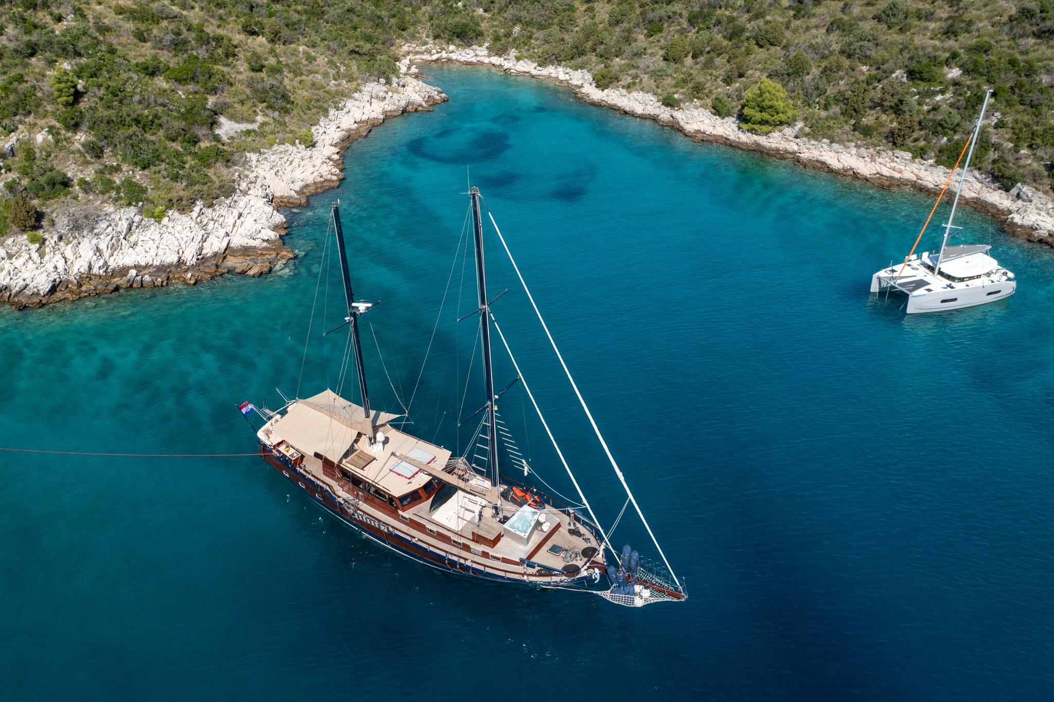 aerial view of traditional wooden gulet anchored in turquoise Mediterranean bay with white catamaran