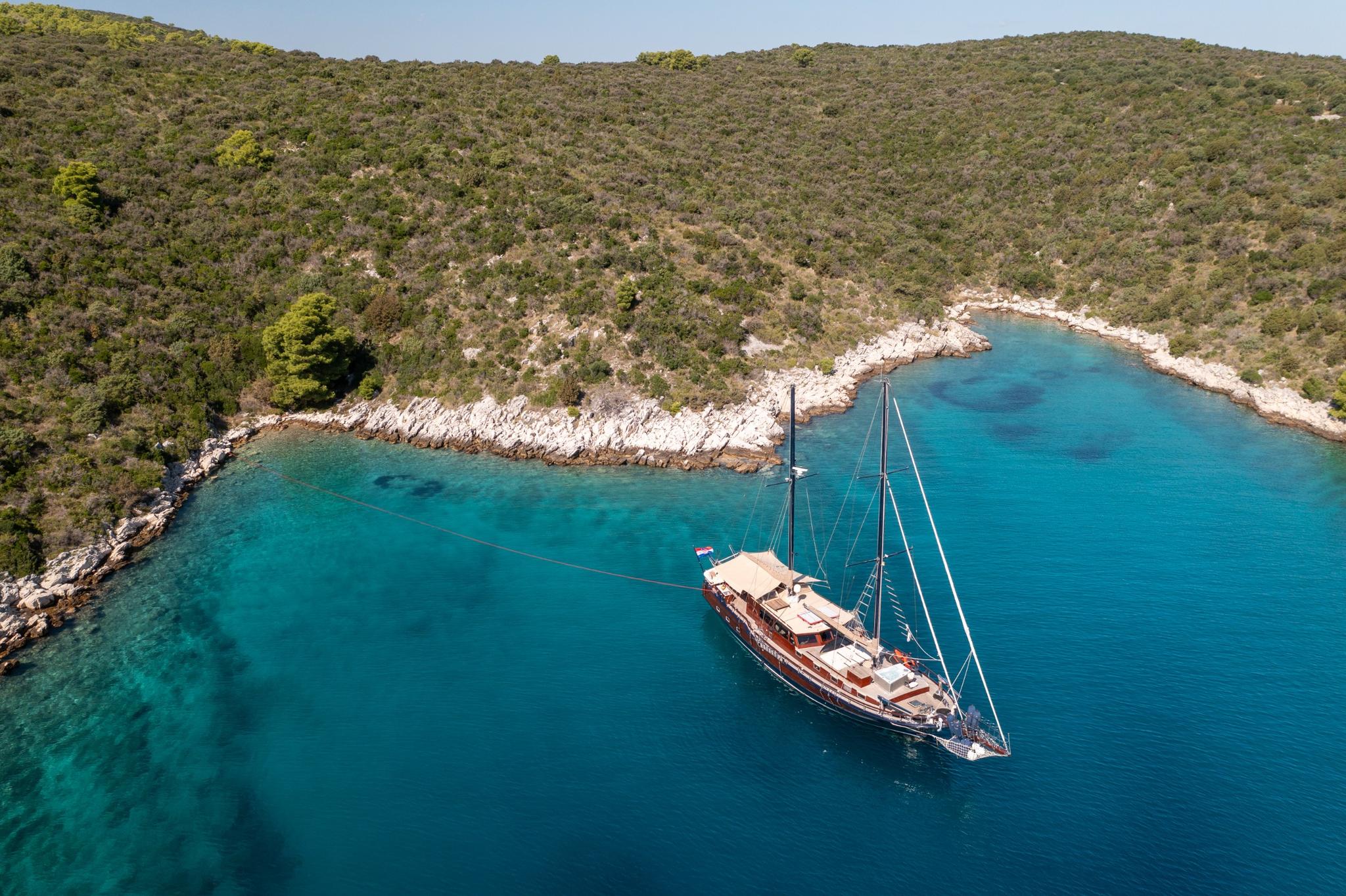 aerial view of traditional wooden gulet anchored in turquoise bay surrounded by forested hills