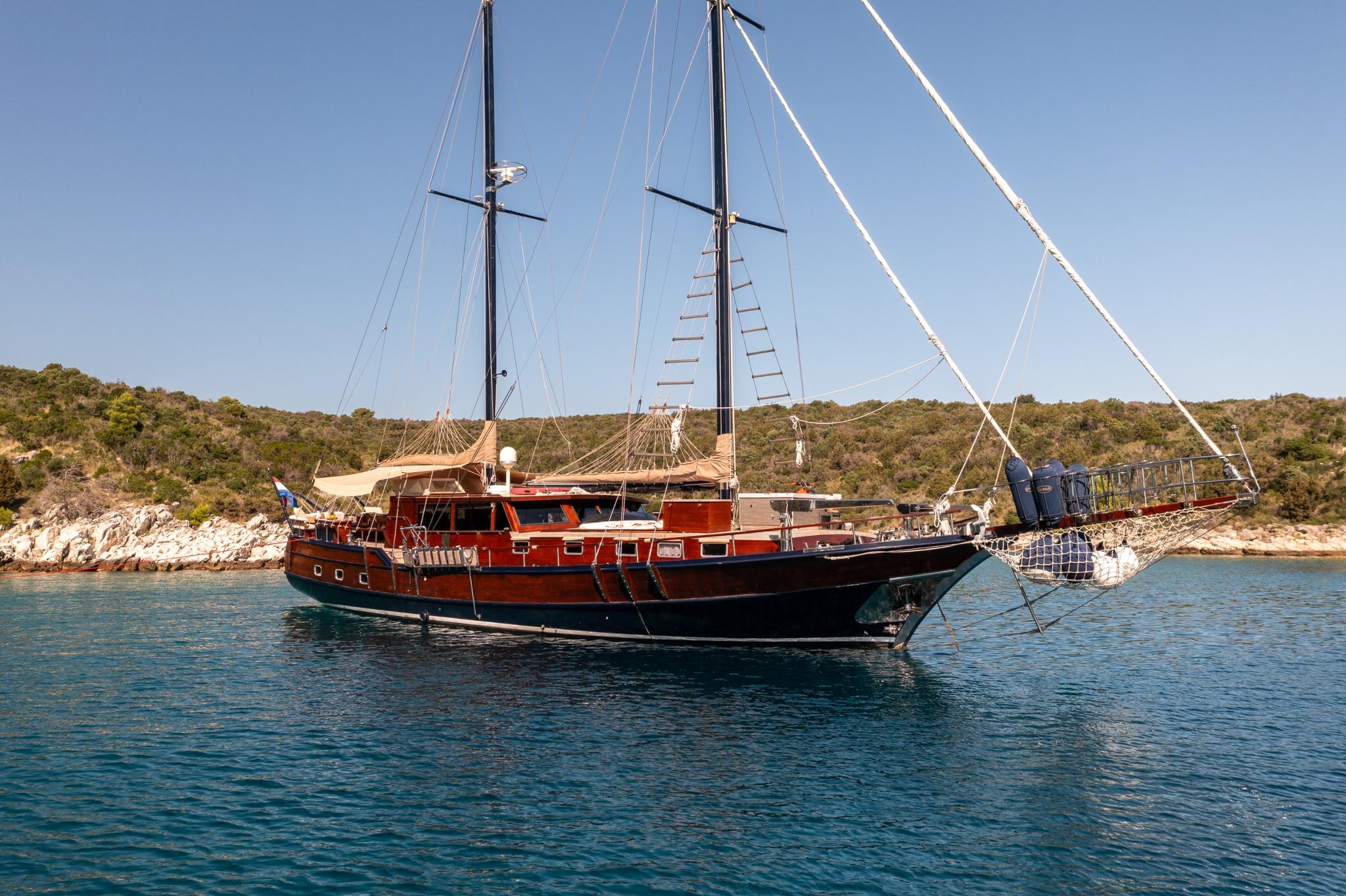 Traditional wooden gulet with red hull and two masts anchored in crystal clear turquoise waters