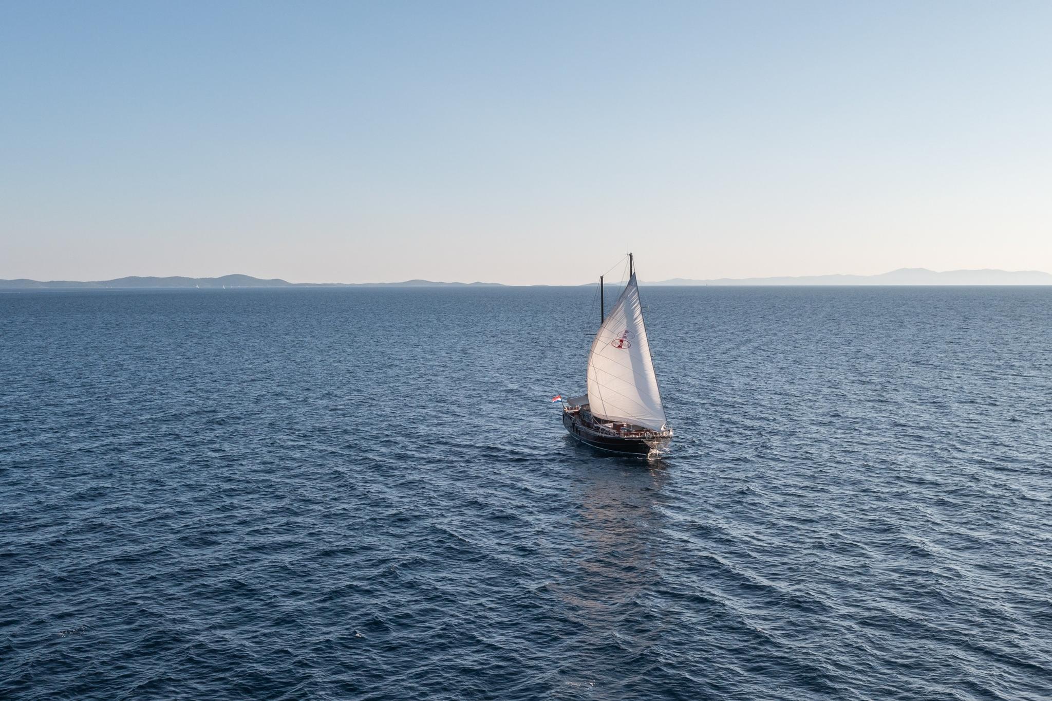 Traditional wooden gulet under sail on blue Mediterranean waters with distant mountains
