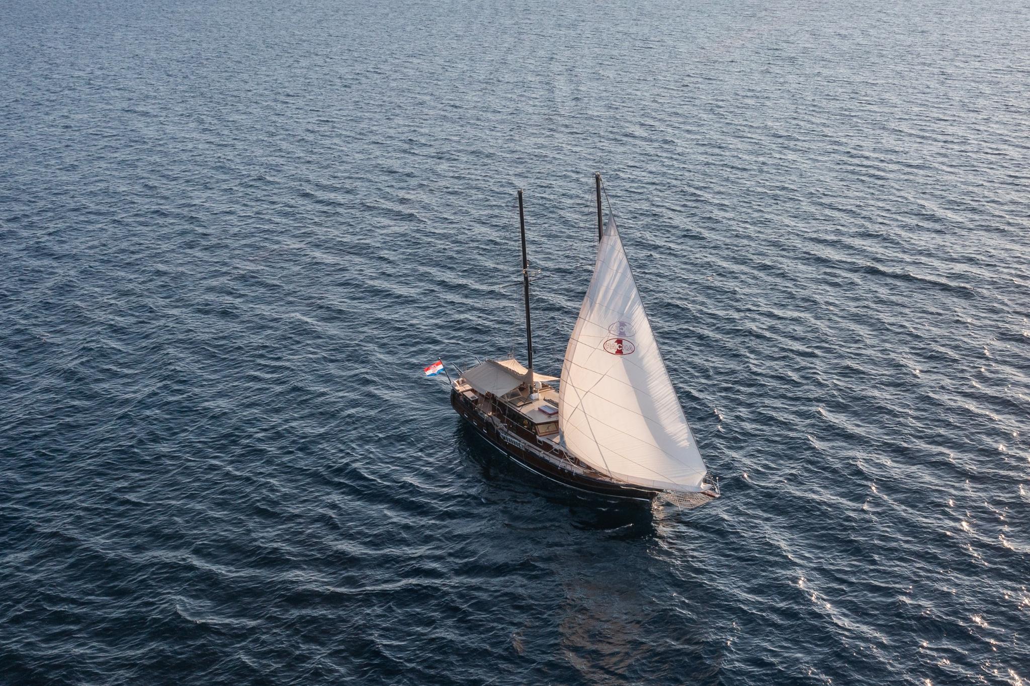 aerial view of traditional wooden gulet sailing with white mainsail deployed on blue water
