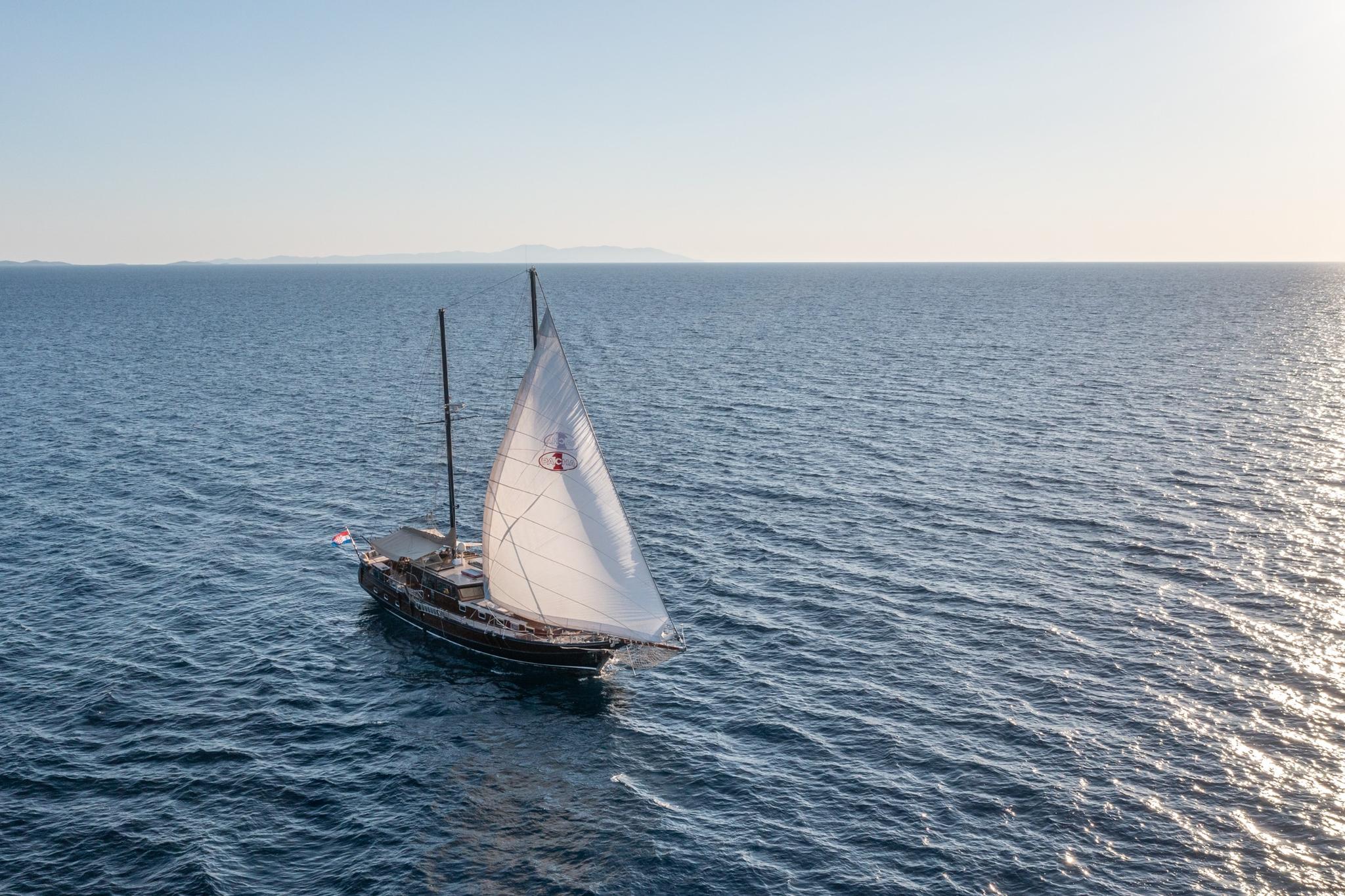 Traditional wooden gulet yacht sailing with white mainsail deployed on blue Mediterranean waters