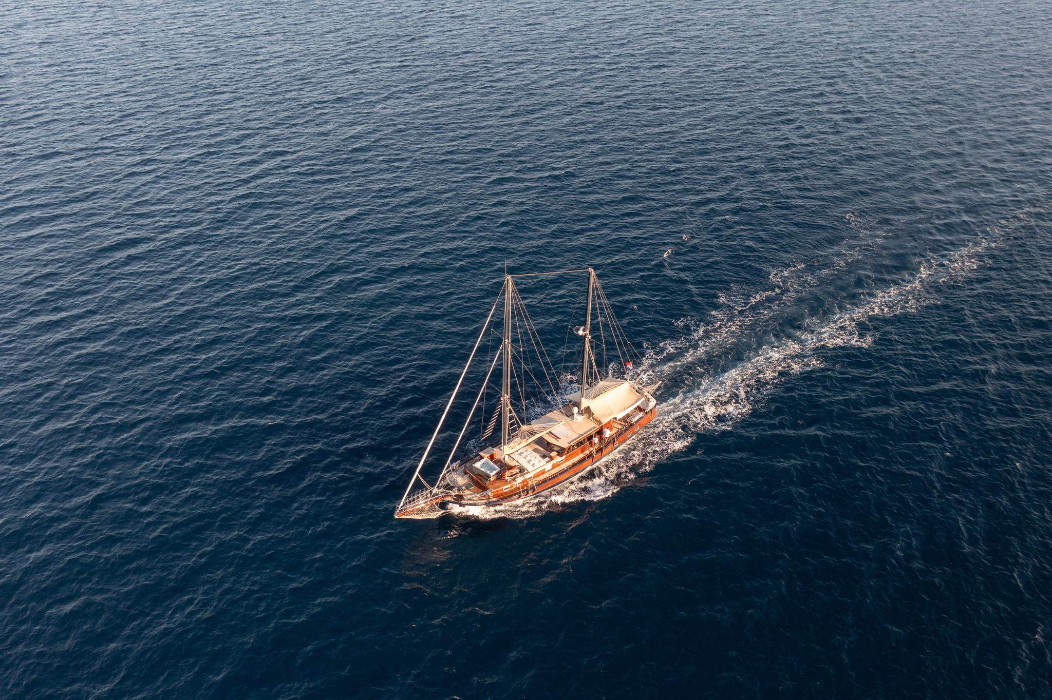 aerial view of traditional wooden gulet with two masts creating wake while sailing